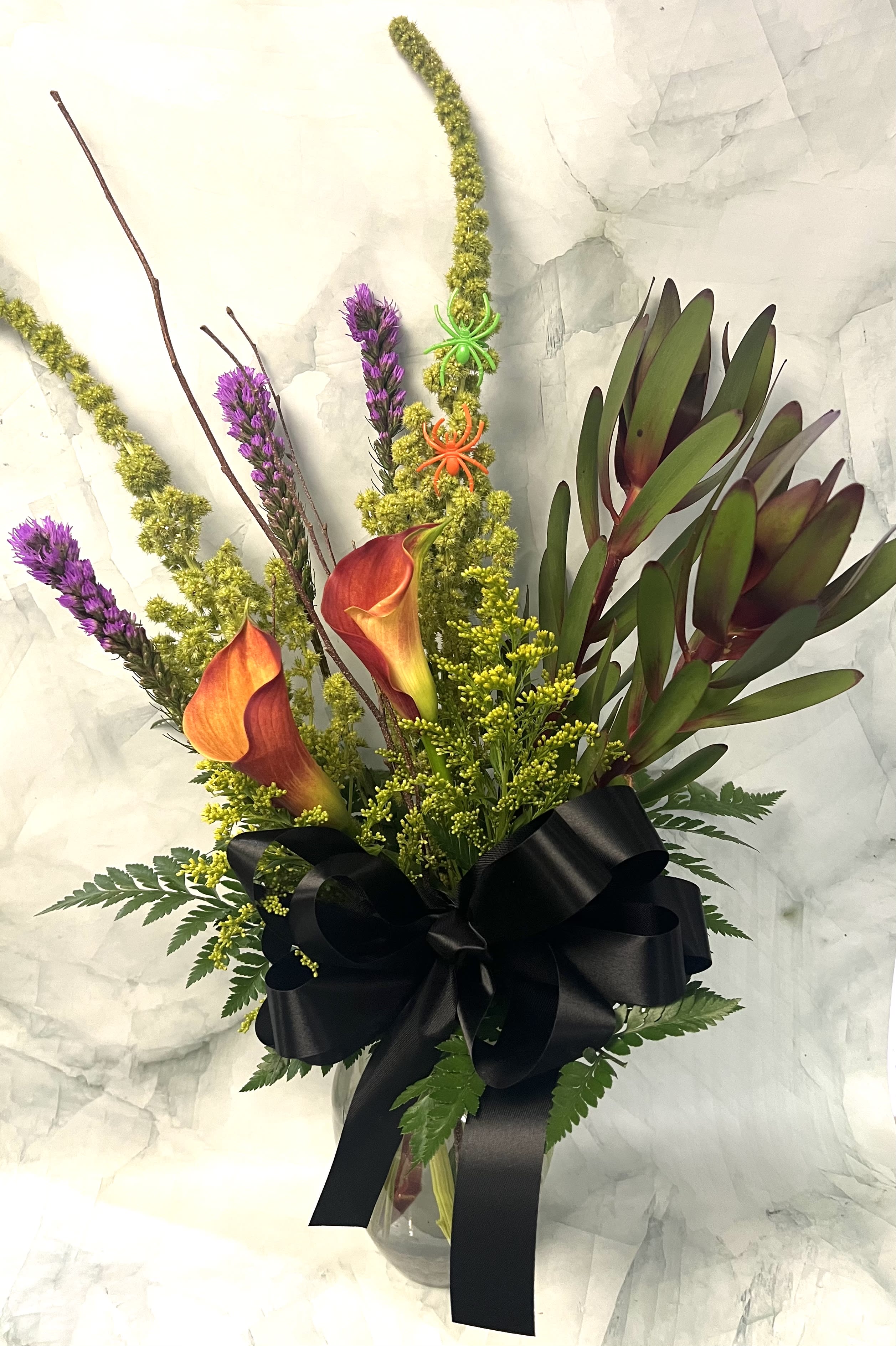 Bouquet of orange calla lilies and purple spikes in a glass vase with a black ribbon