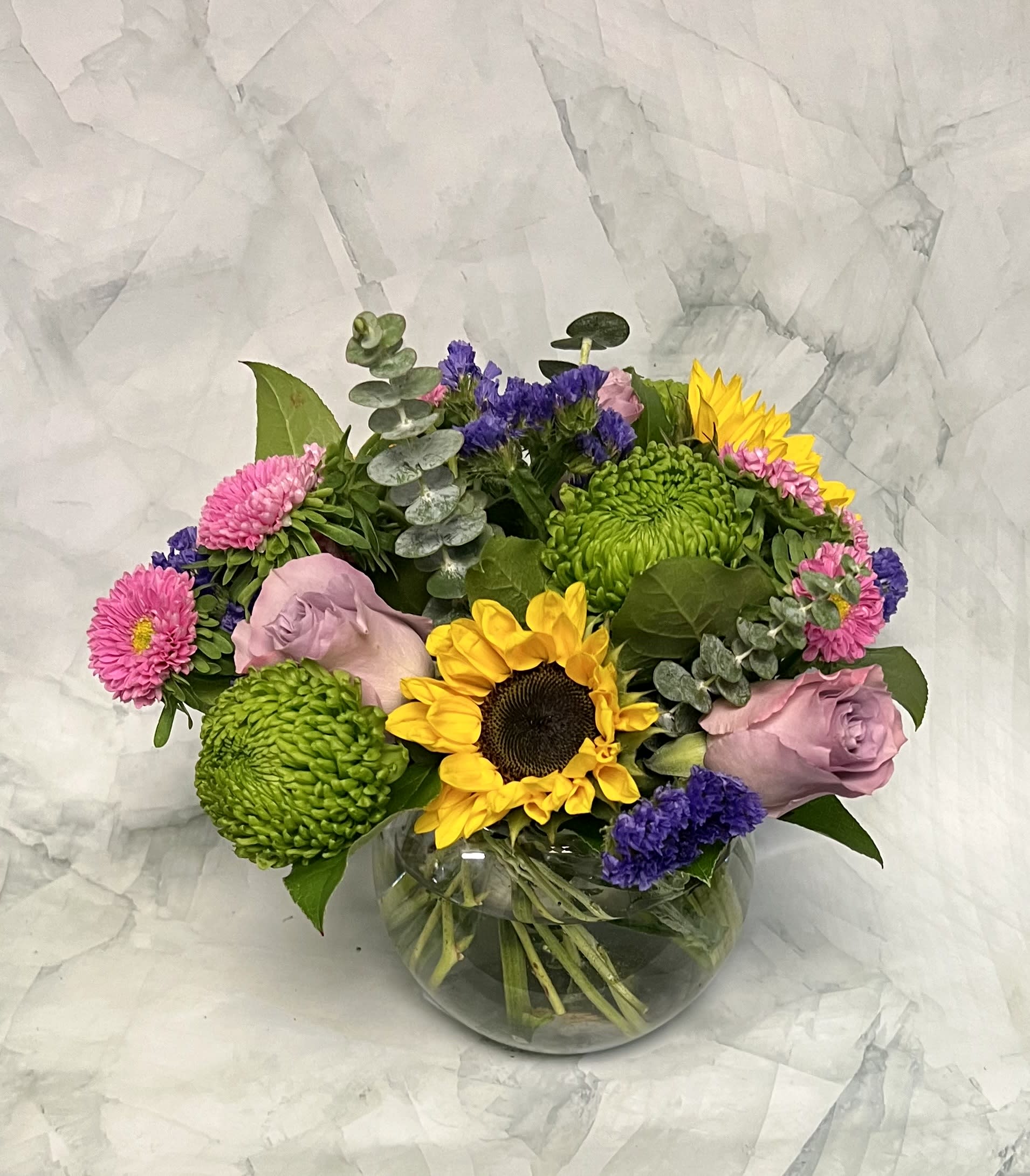 Mixed bouquet with sunflowers, pink roses, and green chrysanthemums in a glass vase