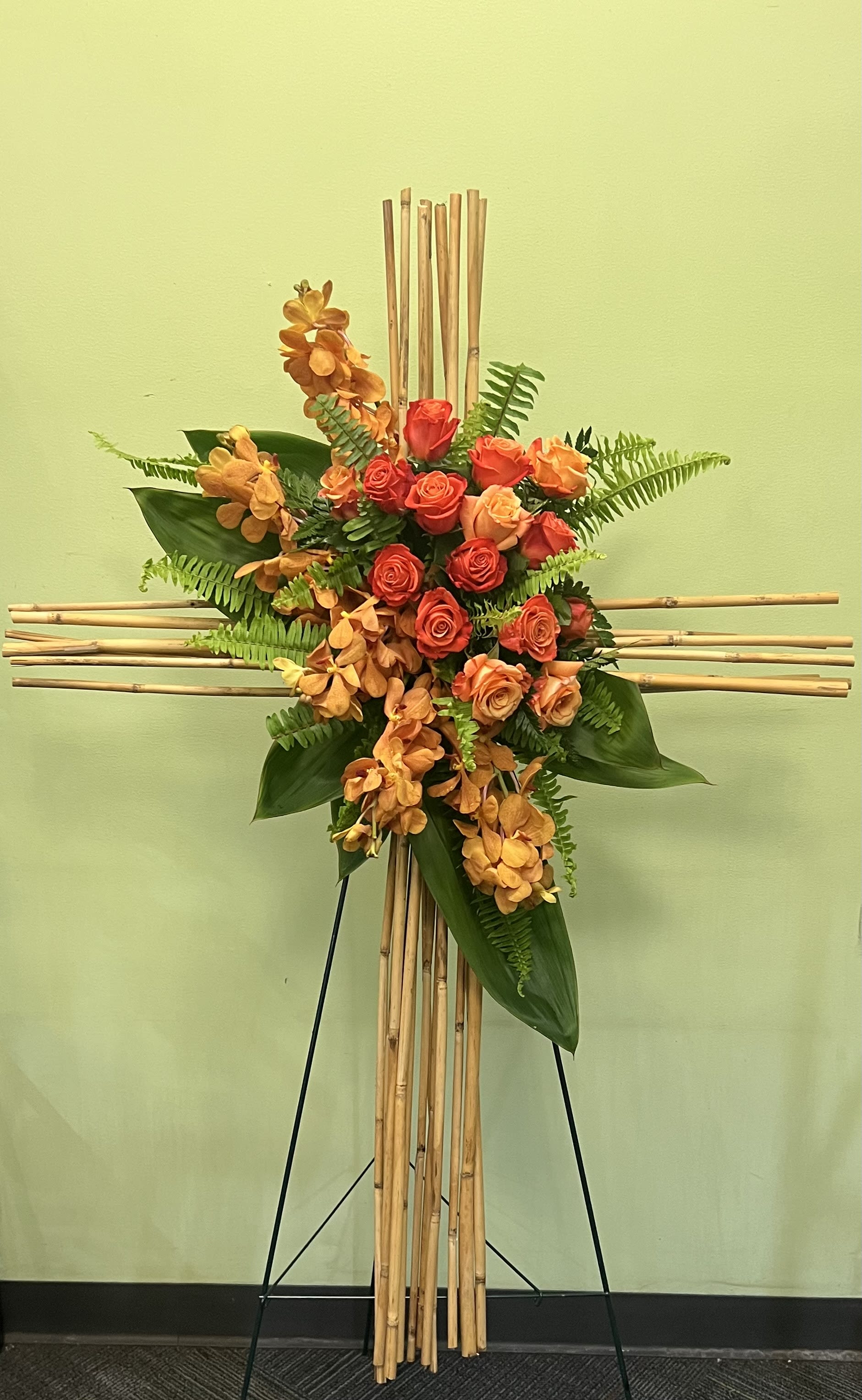 Orange roses and orchids arranged on a bamboo cross stand