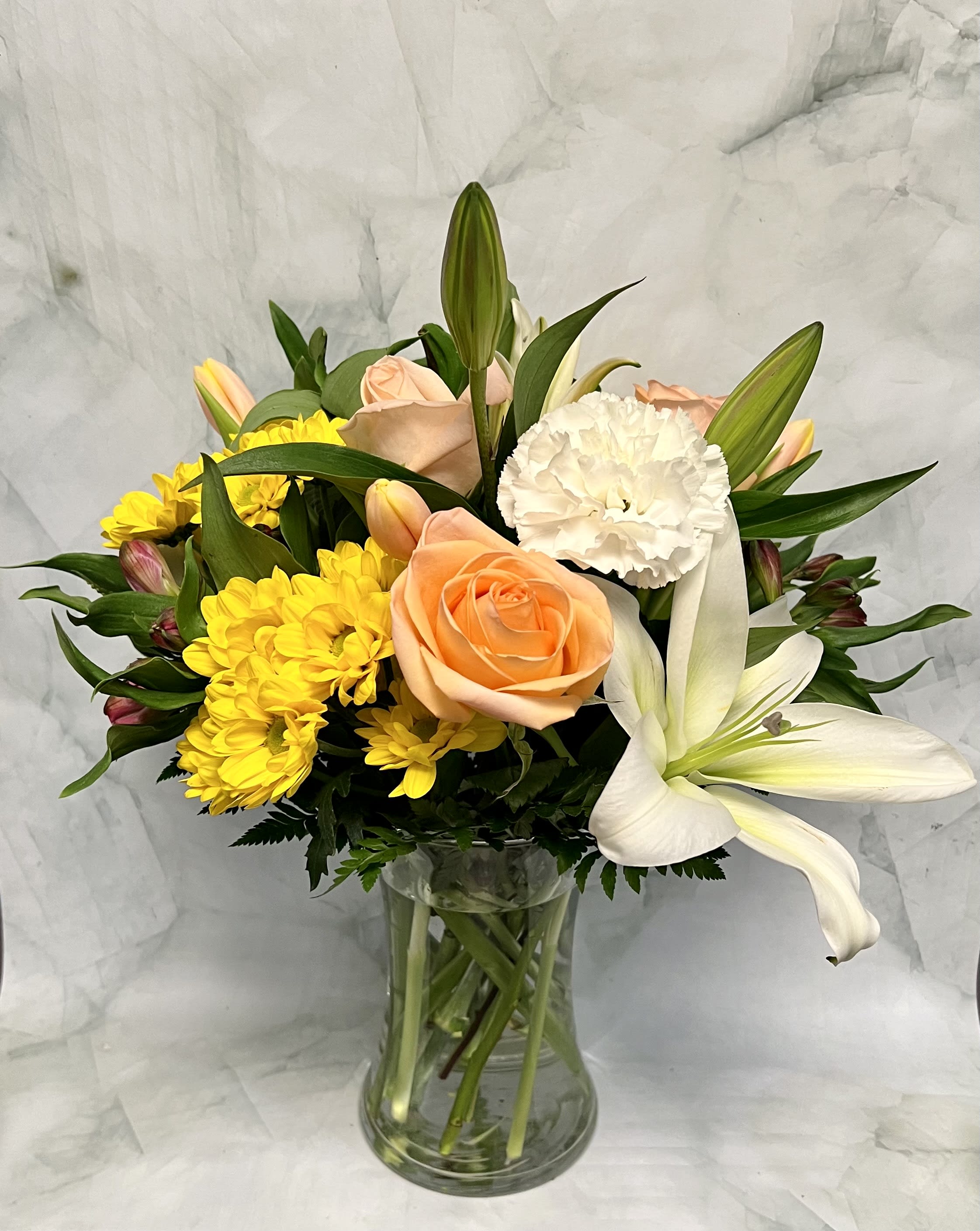 Peach roses, white lilies, and yellow daisies in a glass vase