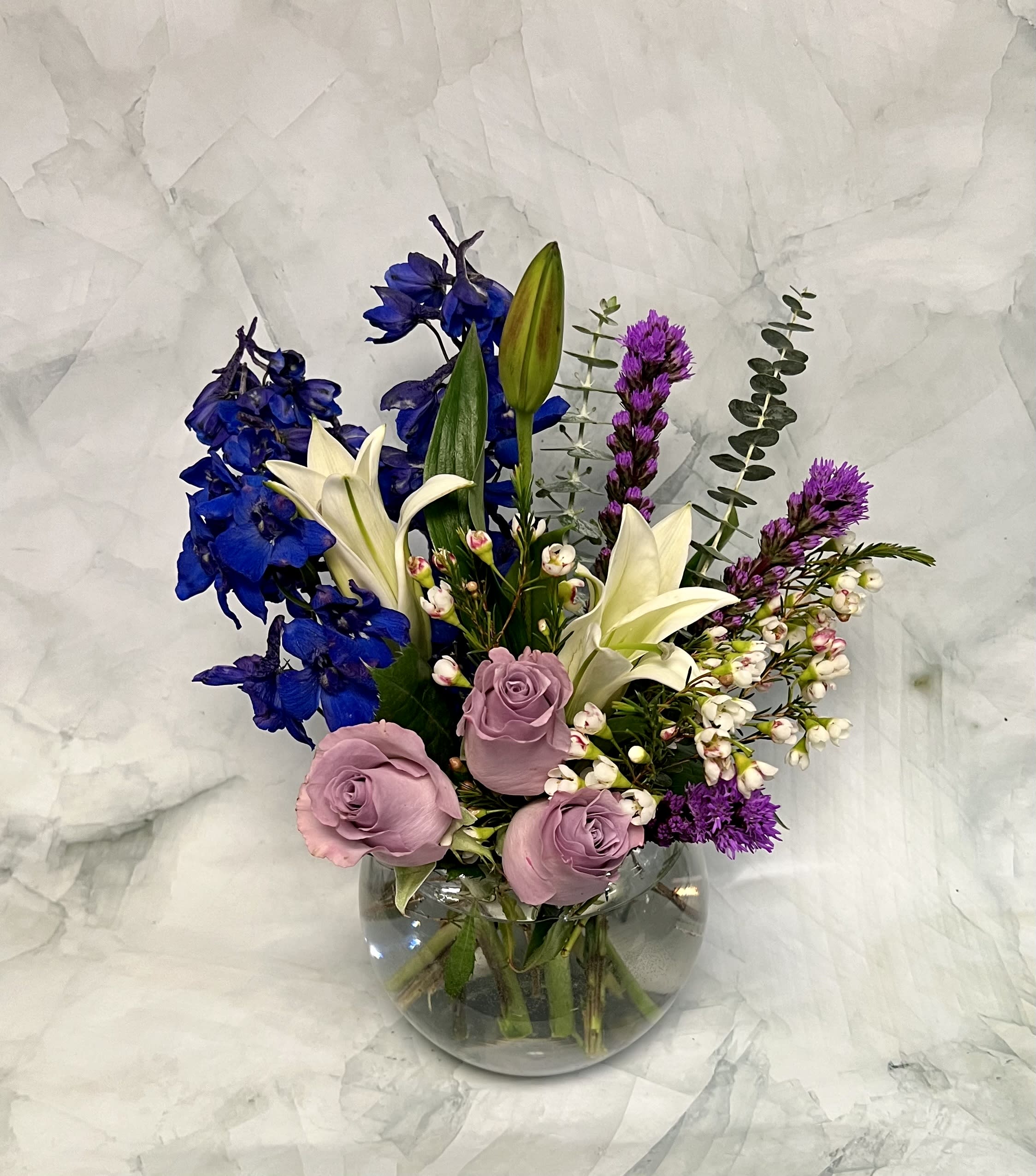 Mixed bouquet in a clear glass vase with blue, white, pink, and purple flowers