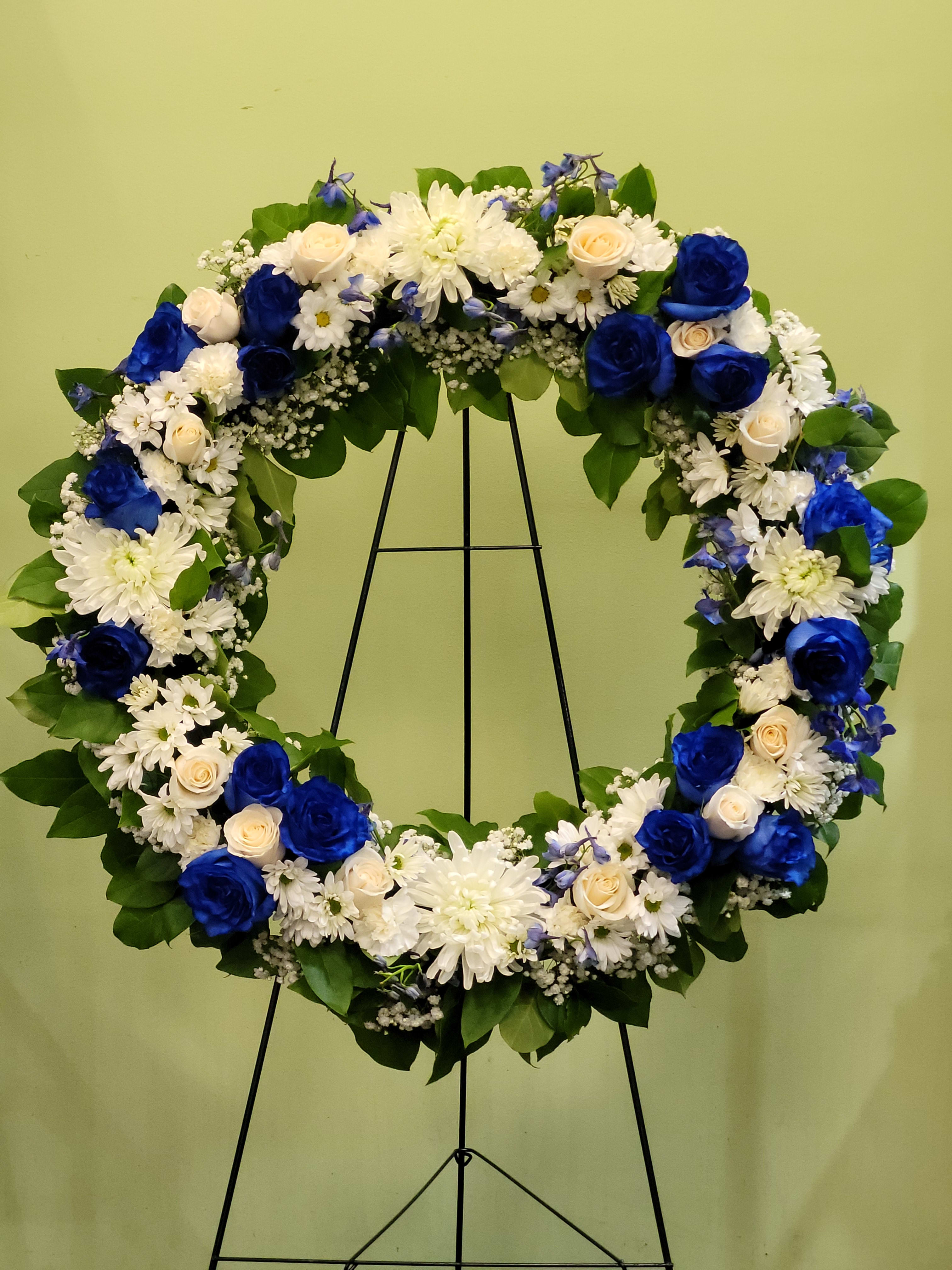 Heart-shaped floral wreath with blue and white flowers on a black stand