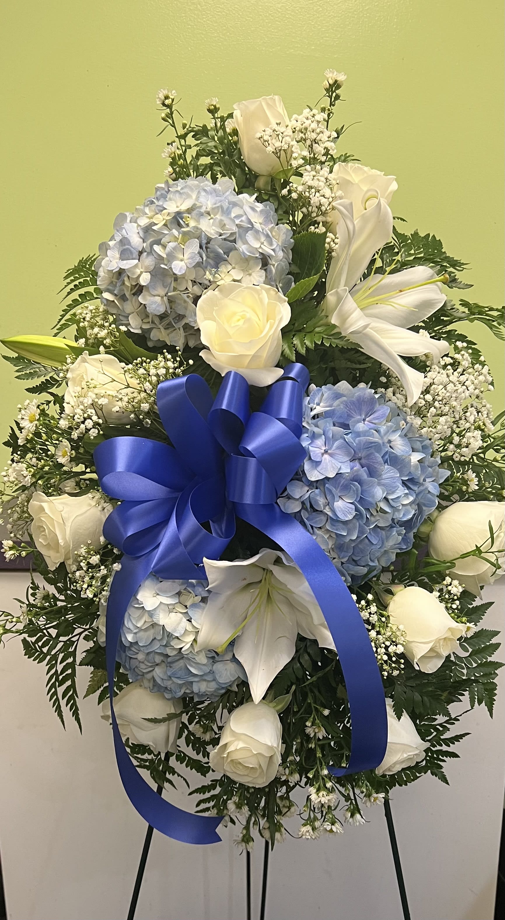 Blue and white floral standing spray with roses, hydrangeas, lilies, and a ribbon bow
