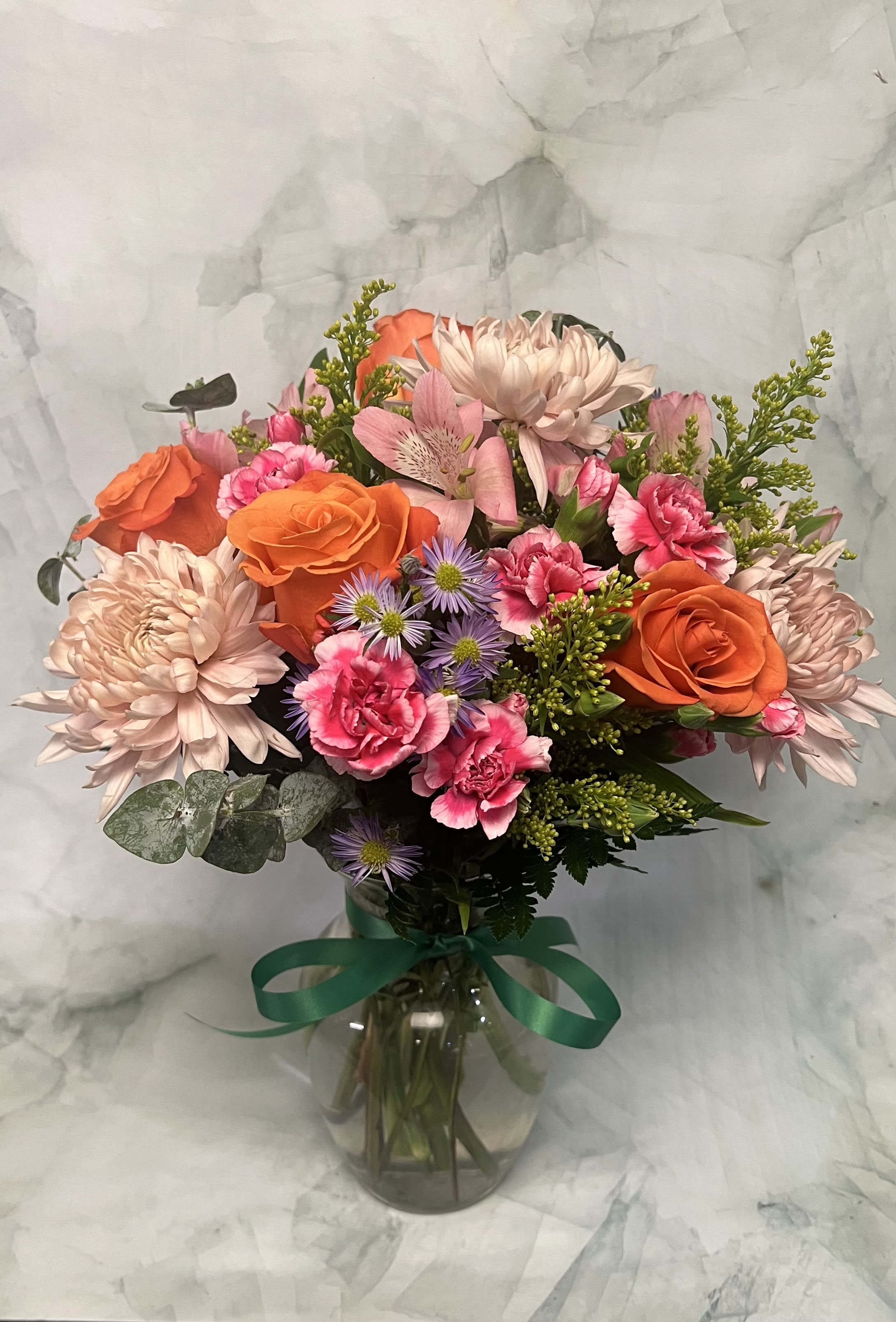 Mixed bouquet of orange roses, pink carnations, and pale chrysanthemums in a glass vase