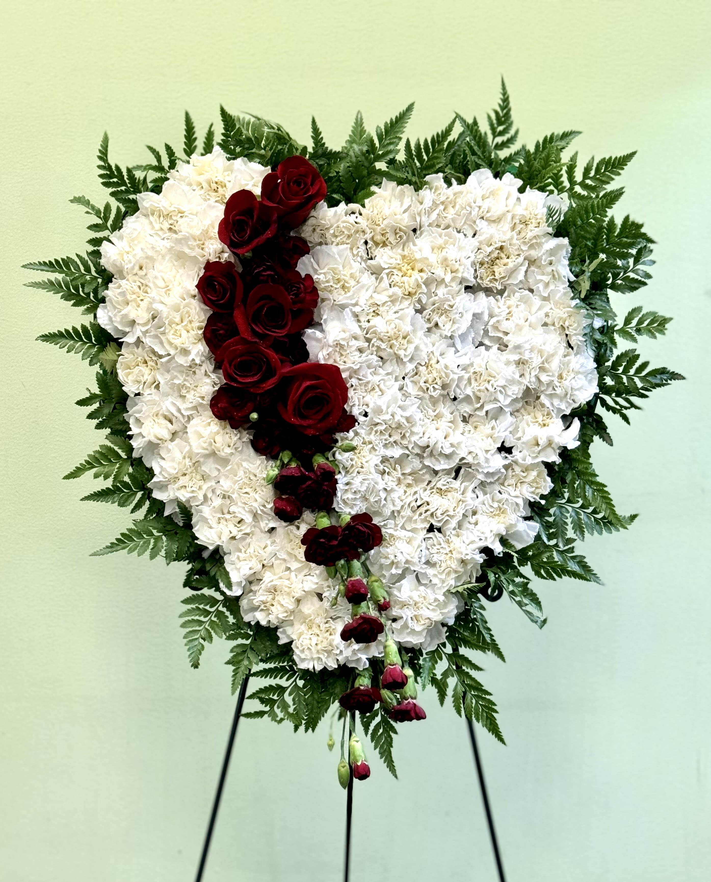 Heart-shaped white floral arrangement with red roses on a stand