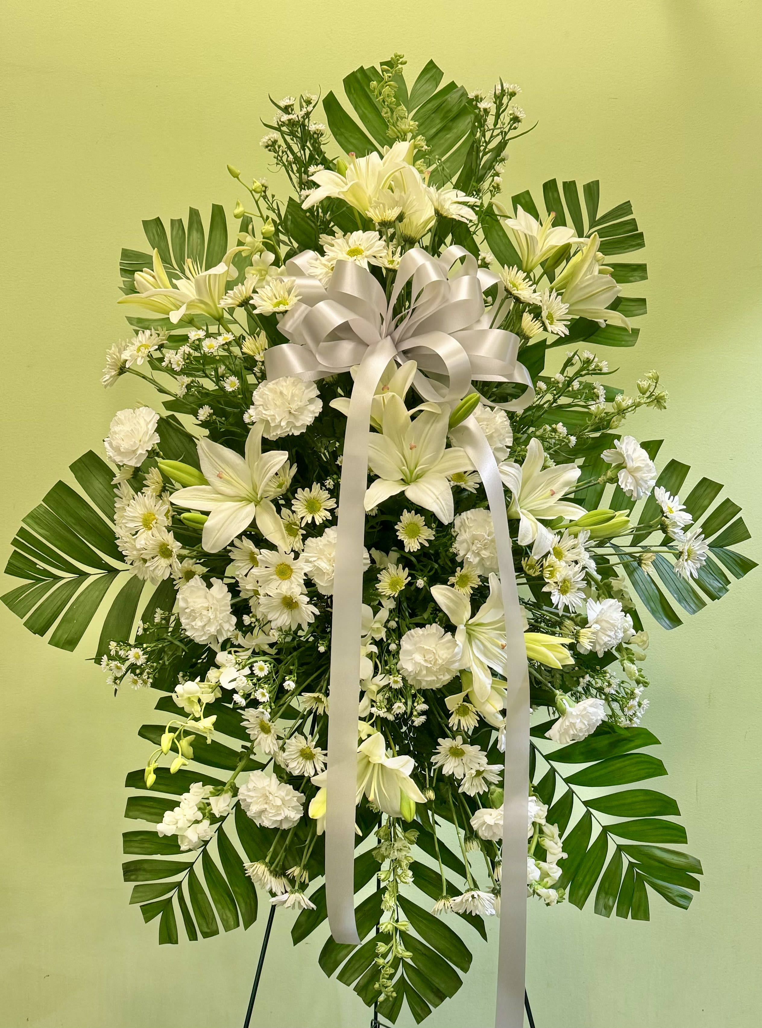 White floral standing spray with lilies, daisies, and a ribbon bow
