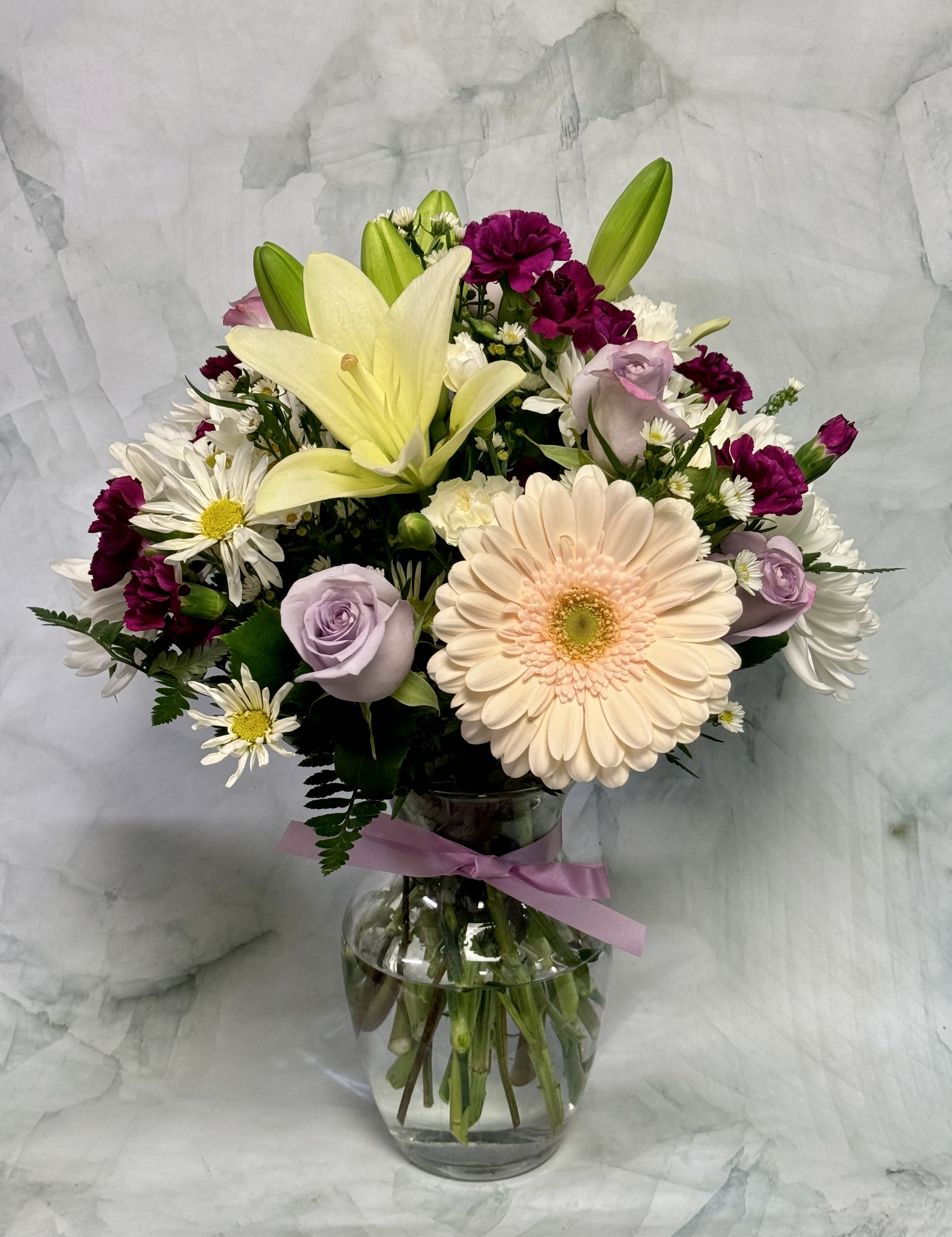 Mixed bouquet with lilies, roses, daisies, and carnations in a glass vase