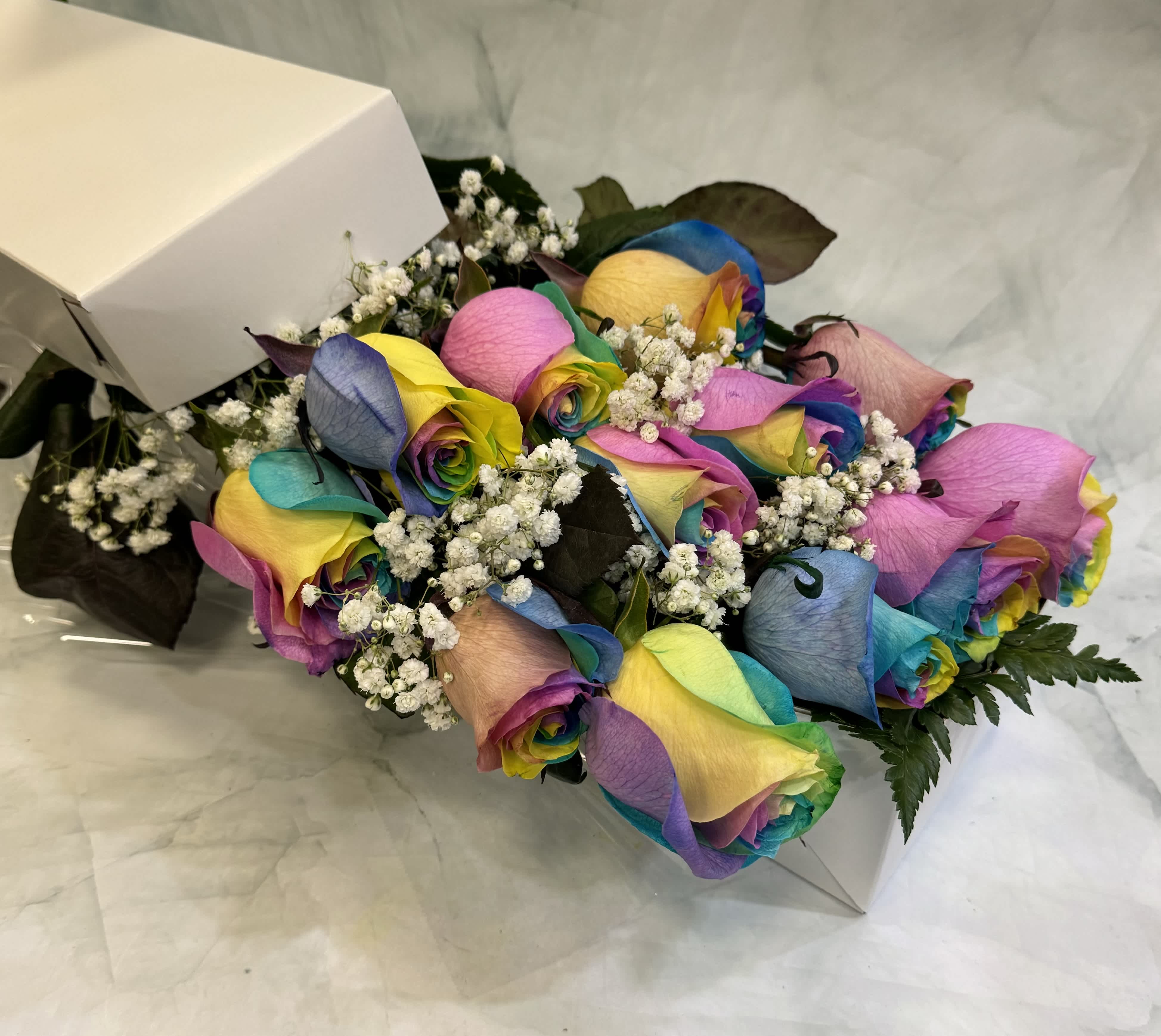 Bouquet of rainbow-colored roses with baby's breath in a white box