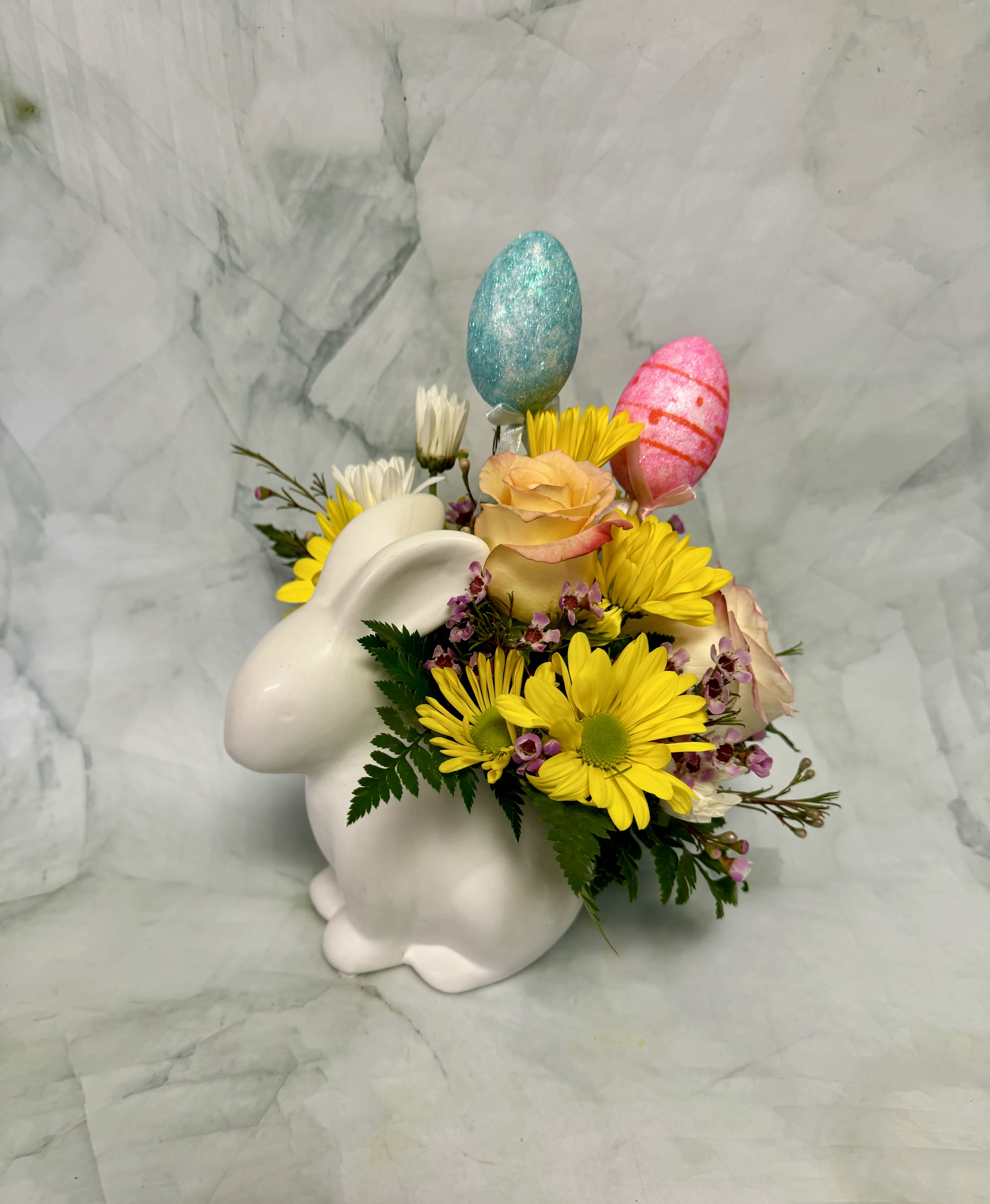 White bunny vase with yellow daisies, peach roses, and pastel decorative egg picks.