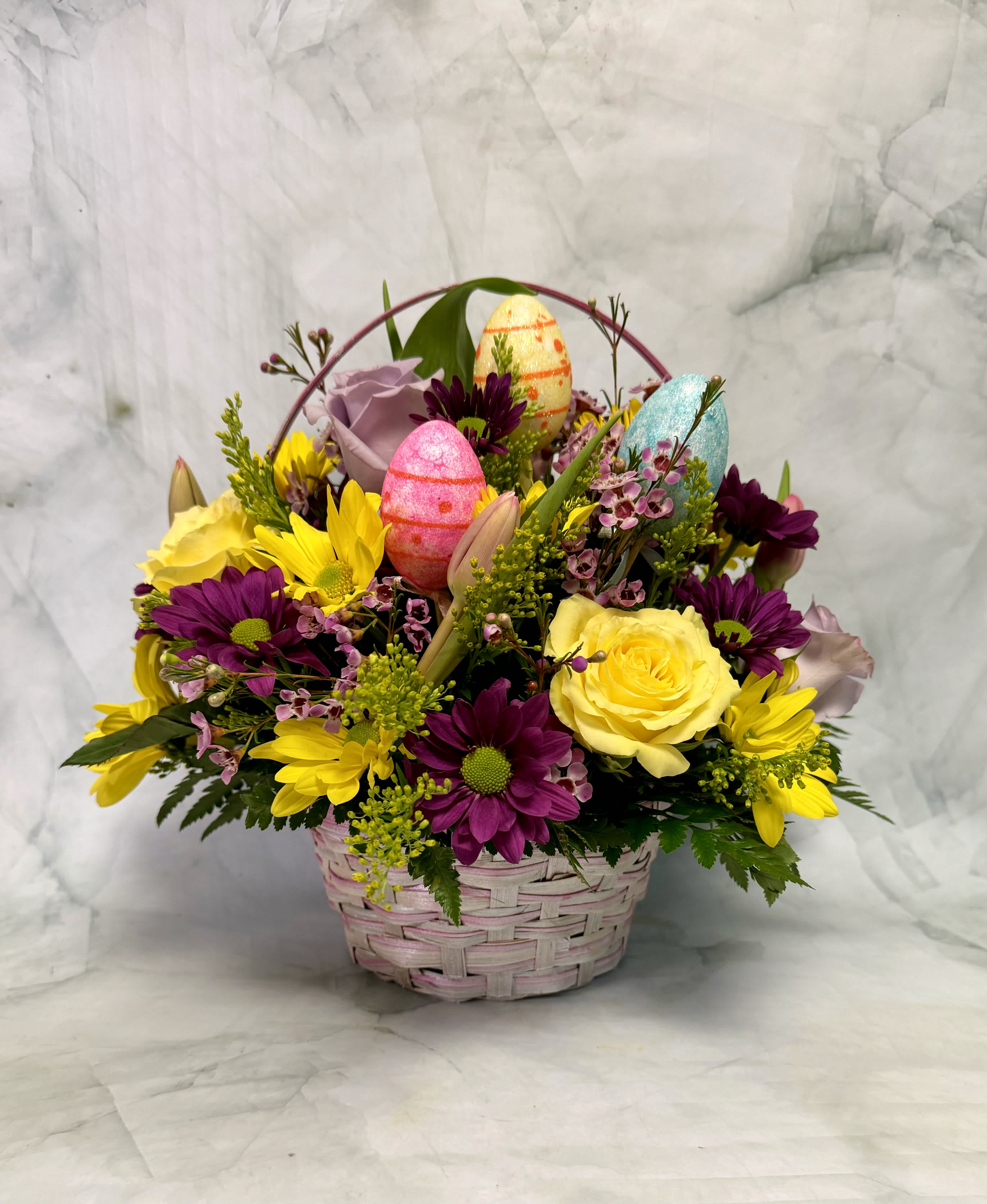 Basket arrangement of yellow and purple flowers with decorative Easter eggs