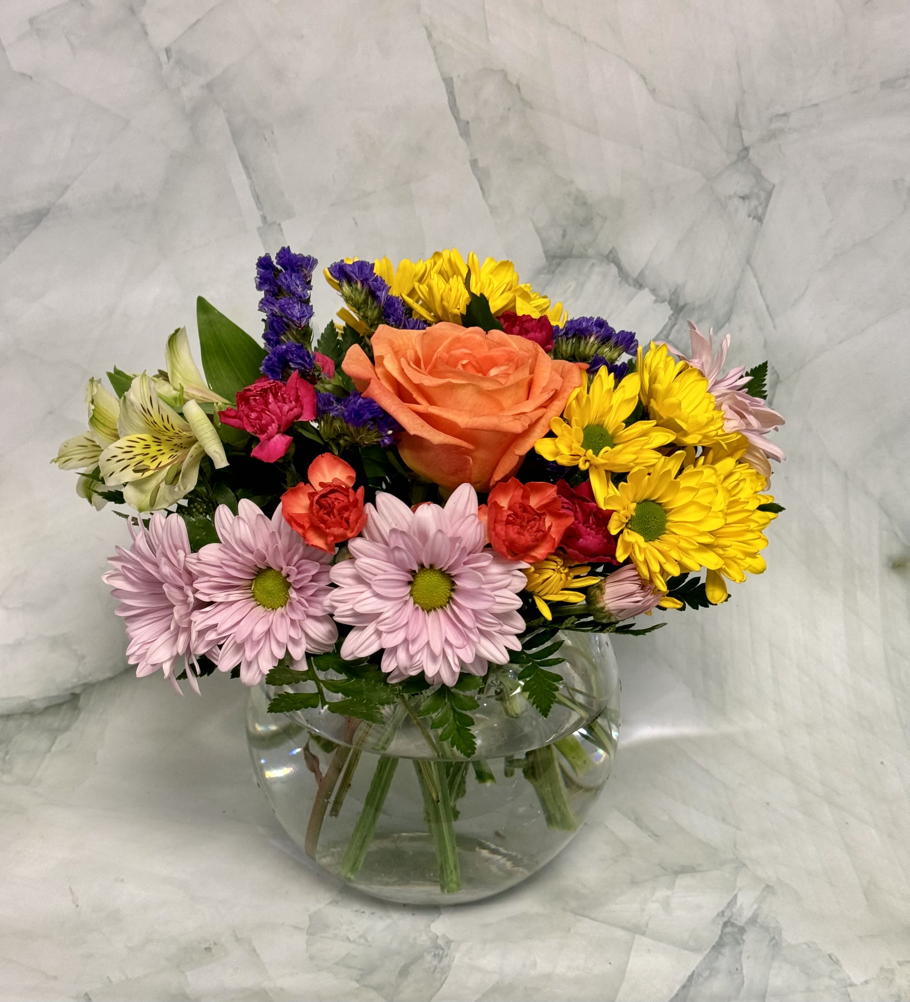 Mixed bouquet in a clear glass vase with an orange rose, daisies, and colorful filler flowers