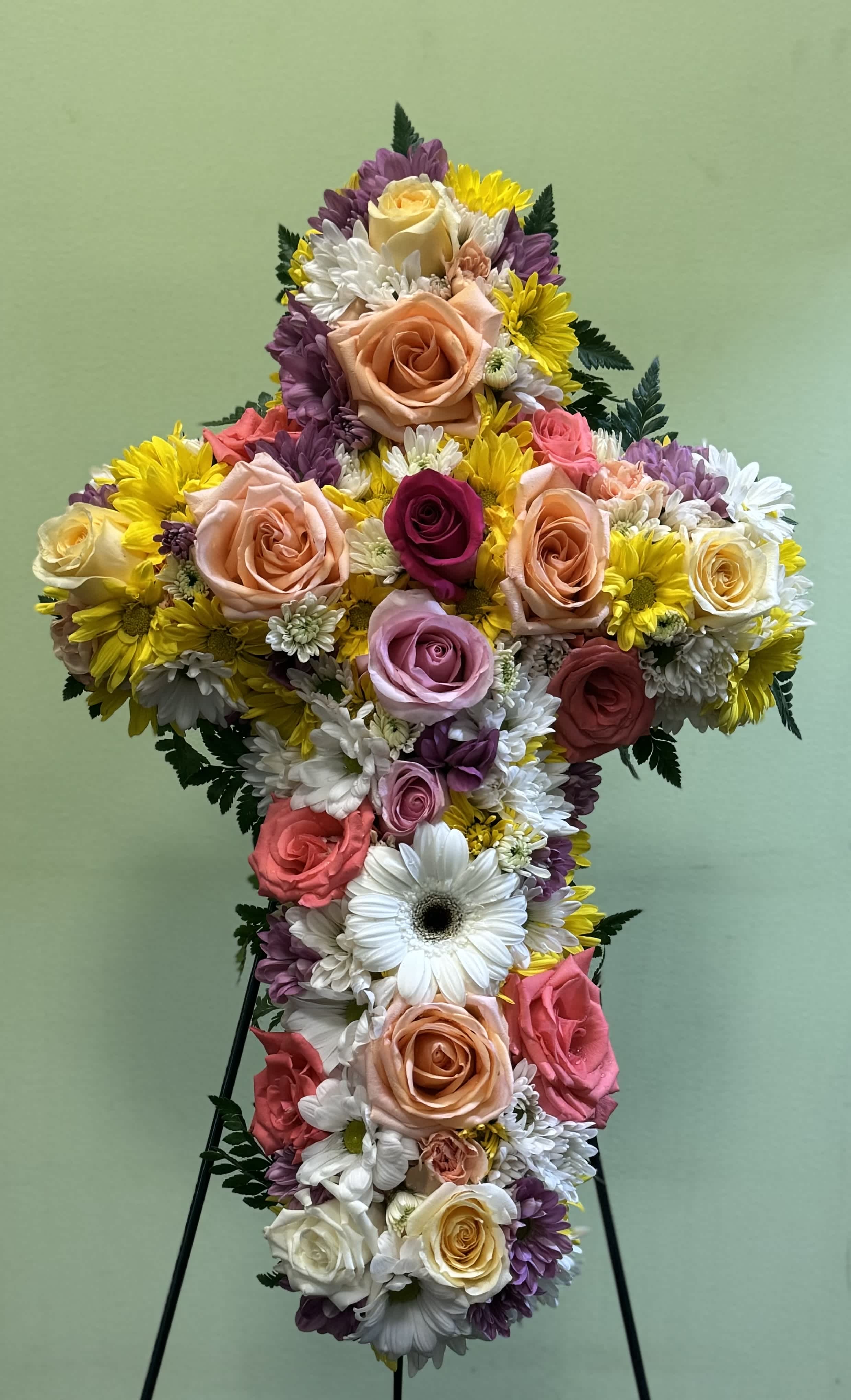 Cross-shaped floral arrangement with roses and daisies on a stand