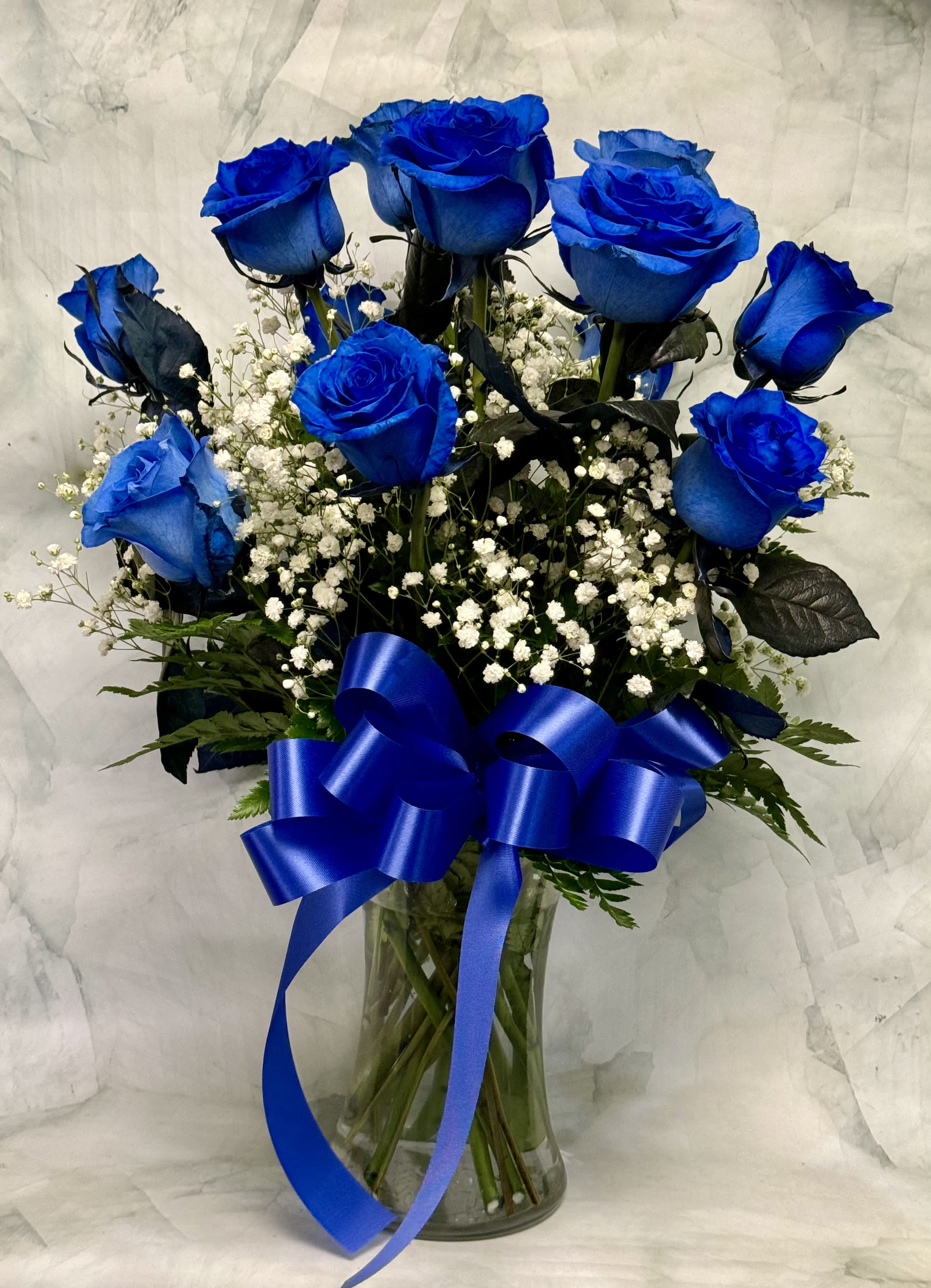 Blue roses in a glass vase with white baby's breath and a blue ribbon