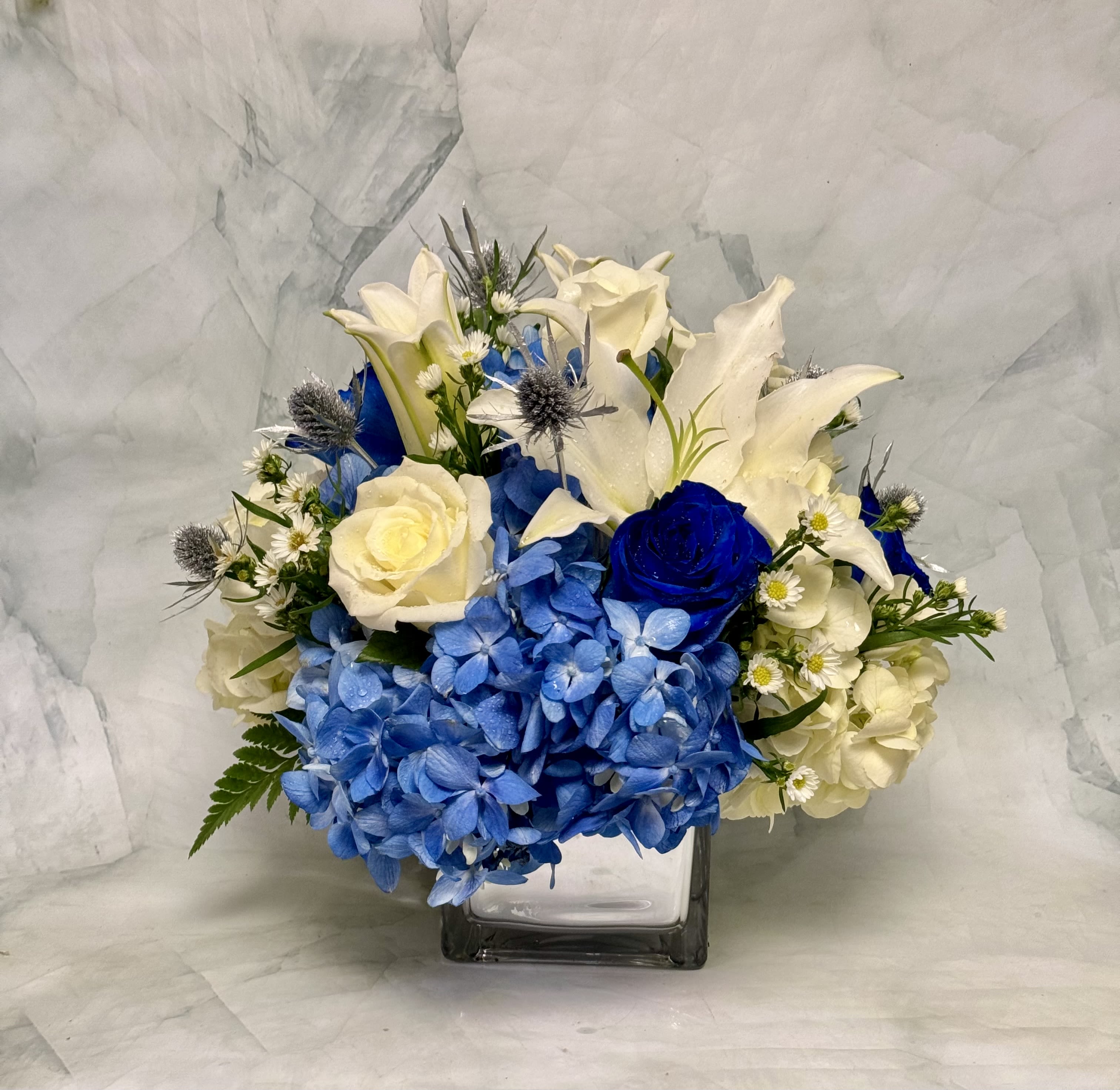 Blue and white floral arrangement in a square glass vase