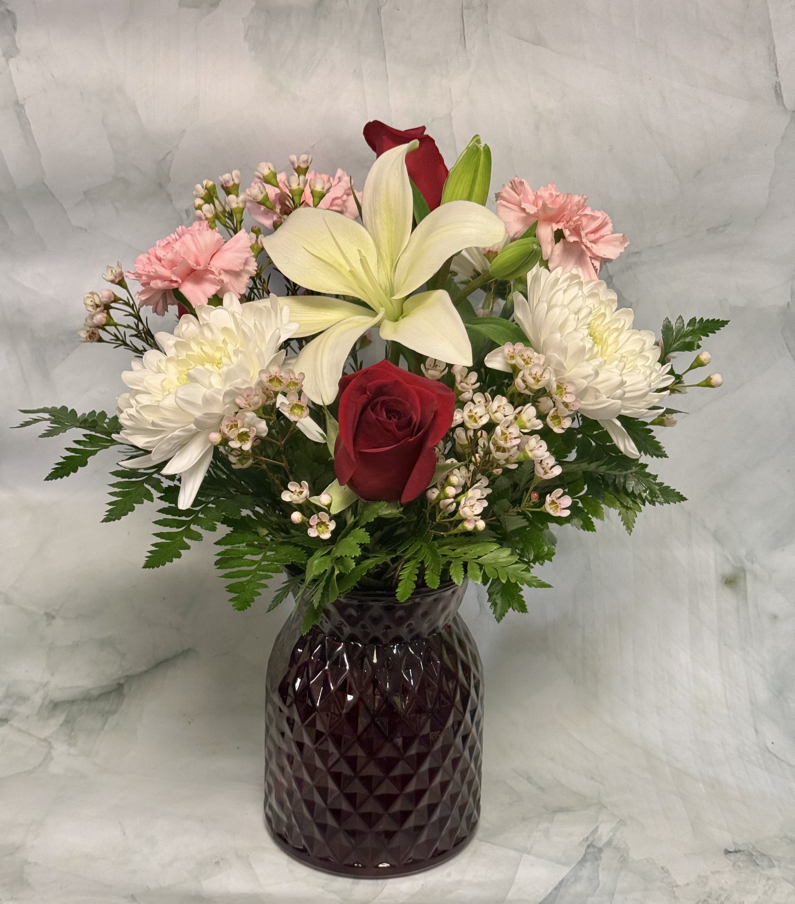 Mixed bouquet with red roses, white lilies, and pink carnations in a dark vase