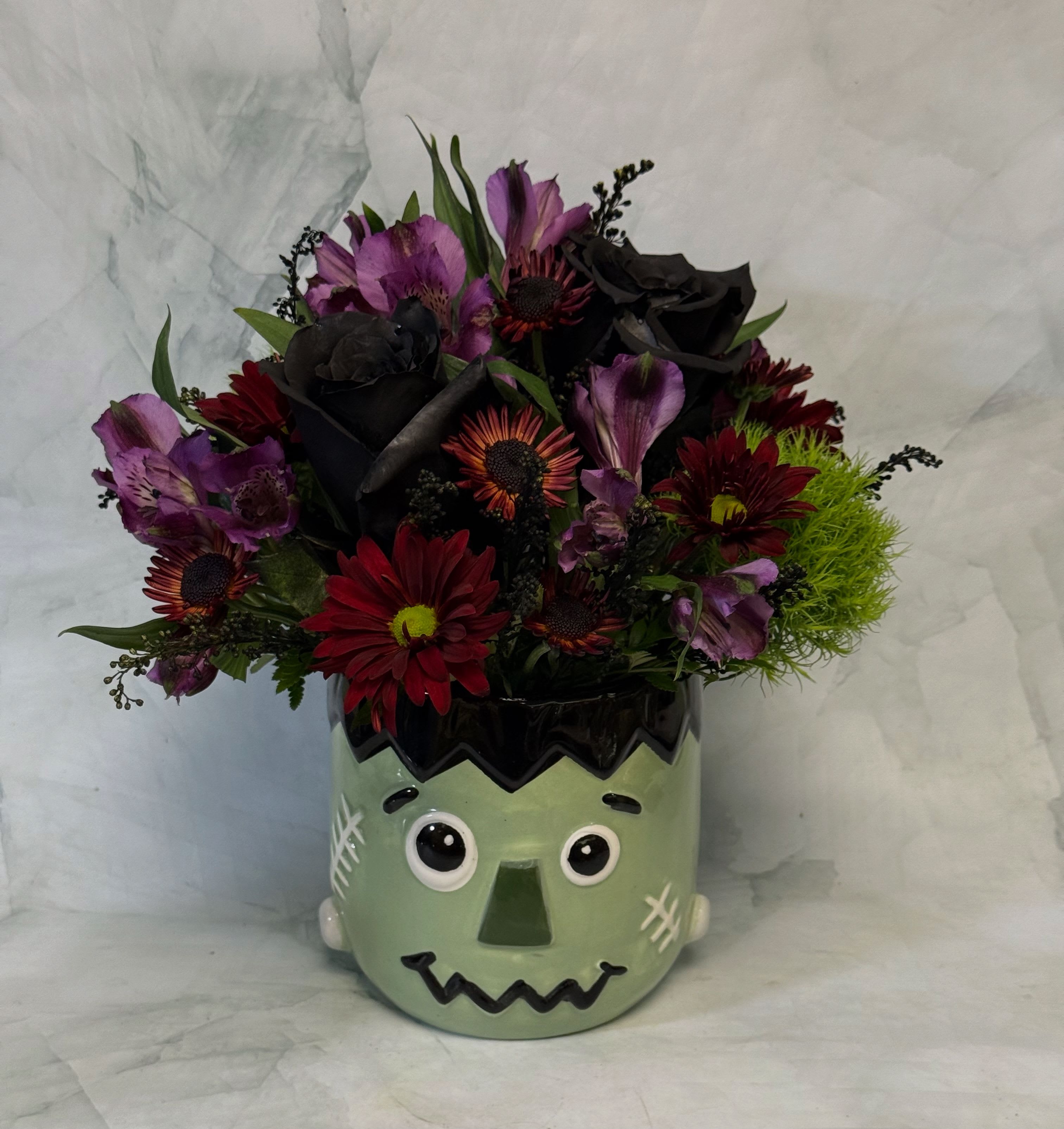 Bouquet of red, purple, and black flowers in a Frankenstein face vase