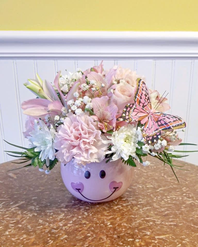 Pastel flower arrangement in a smiley-face ceramic pot with a butterfly accent