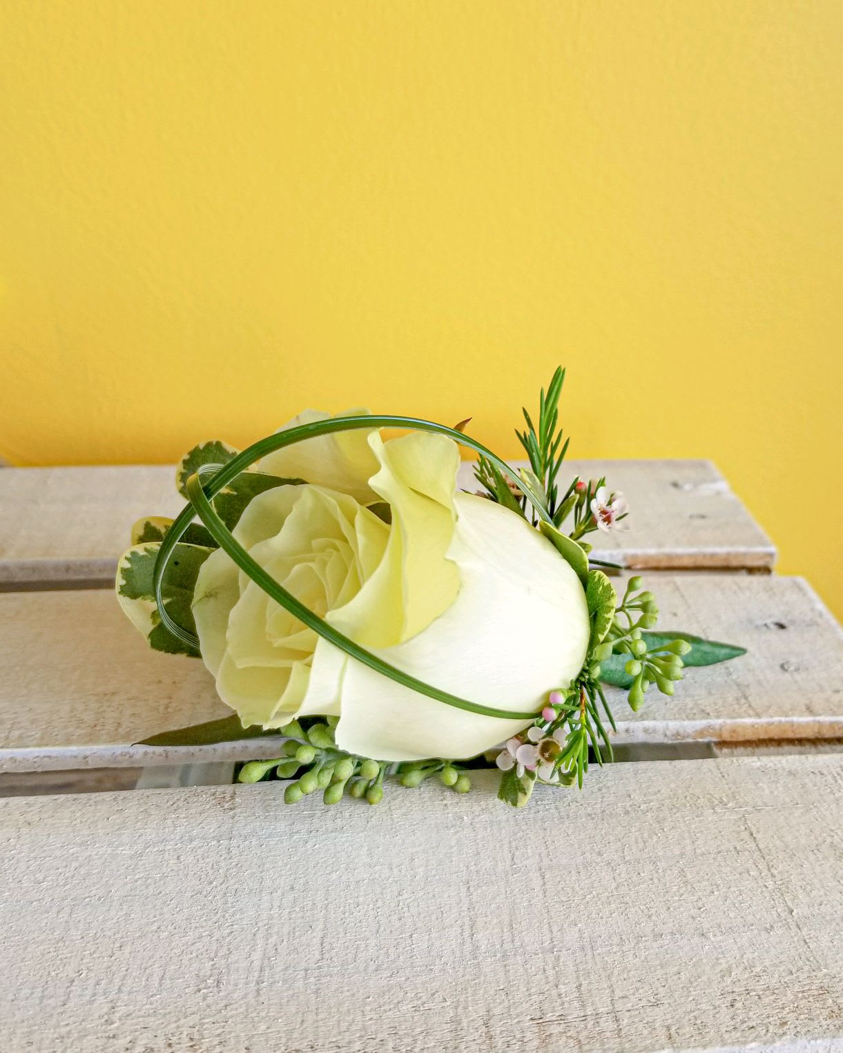 White rose boutonniere with small green accents on a wooden surface
