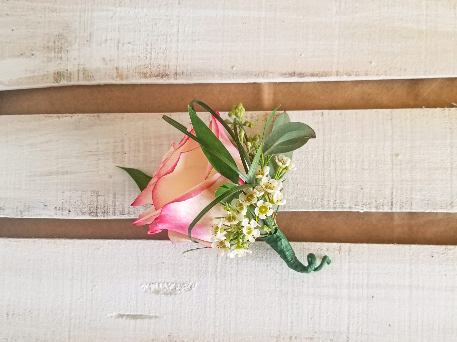 Pink rose boutonniere with small white flowers and greenery