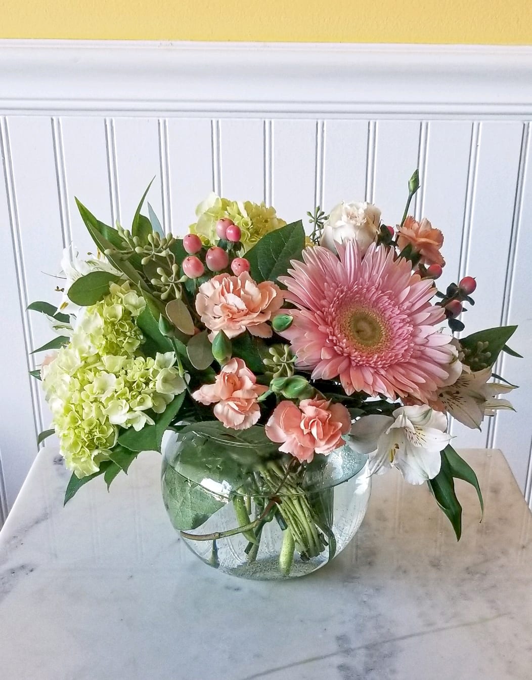 Pink gerbera and peach carnations in a round glass vase
