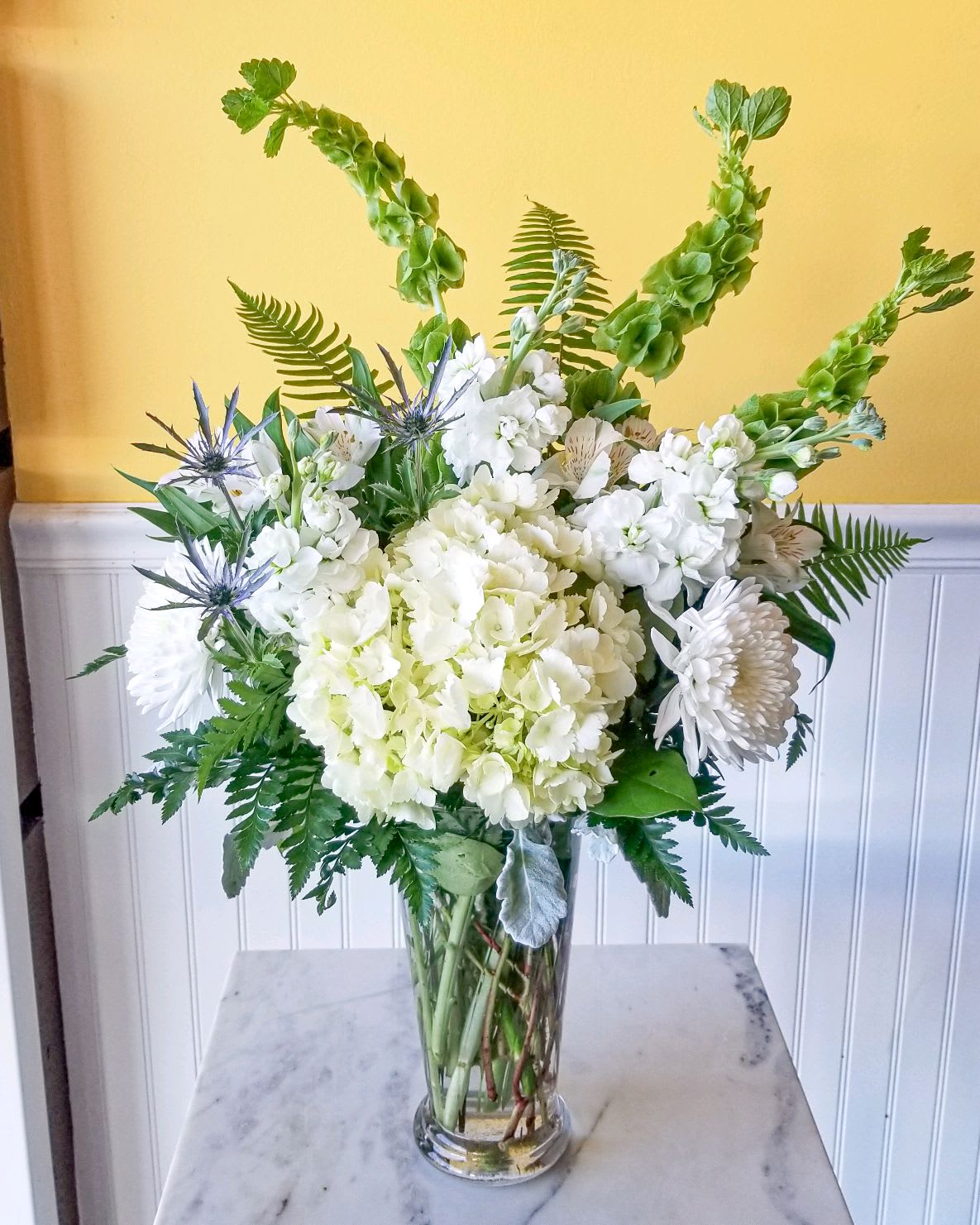 White floral arrangement in a clear glass vase with tall green spikes