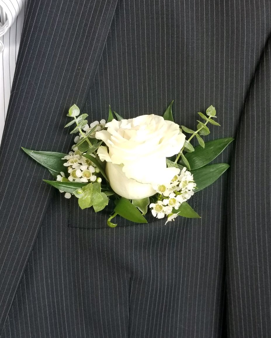 White rose boutonniere with small white filler flowers and greenery