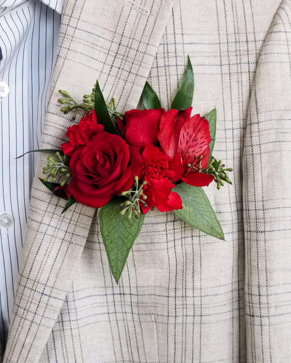 Red rose boutonniere with green leaves on a plaid jacket