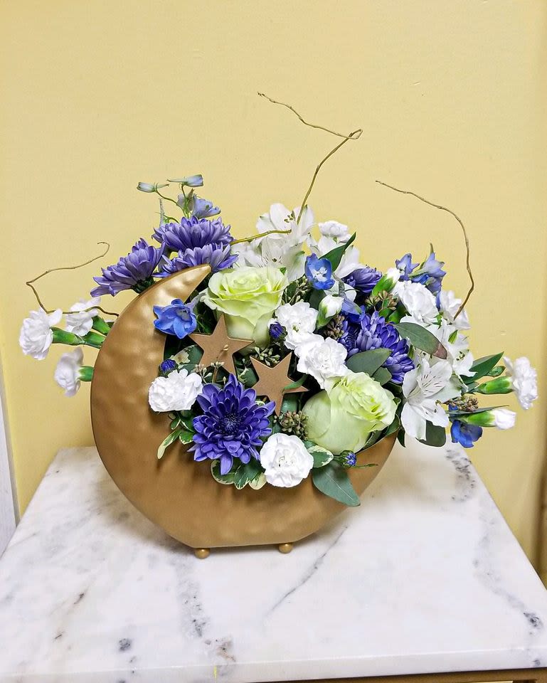 Purple and white floral arrangement in a gold crescent vase with star accents