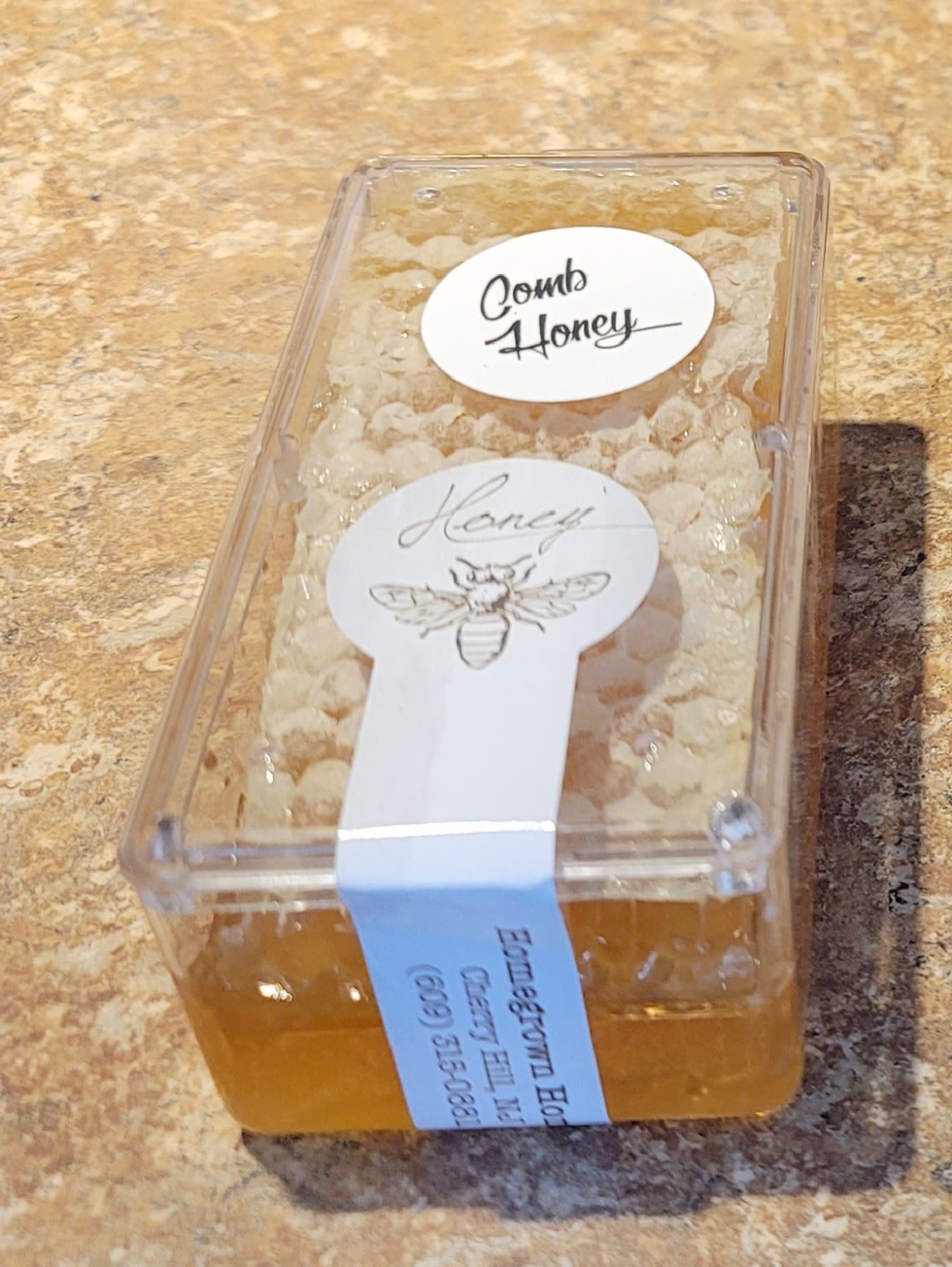 Plastic container of comb honey with labels on a countertop