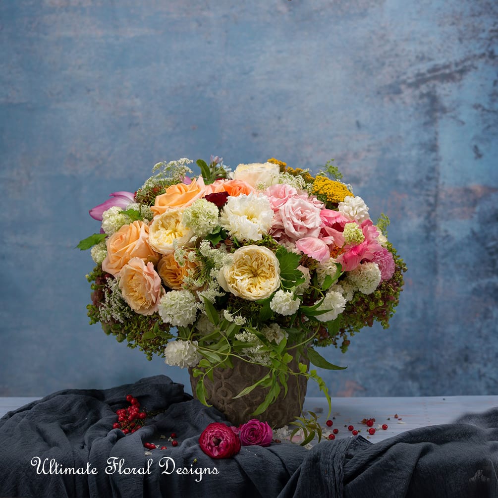 Mixed bouquet of peach, pink, white, and yellow flowers in a decorative vase