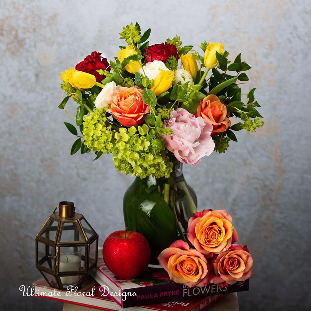 Mixed bouquet of roses and other blooms in a green glass vase