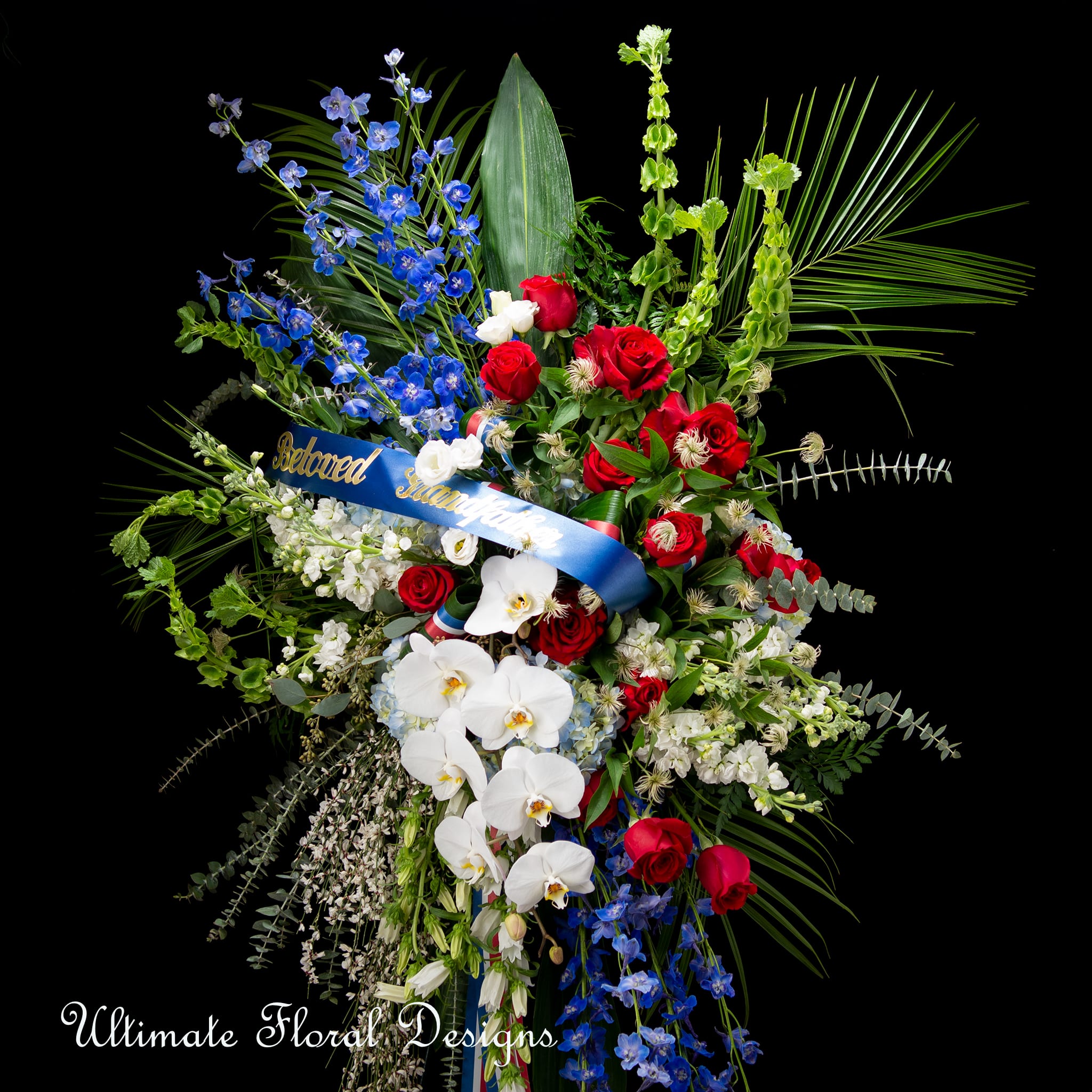 Large standing floral spray with red roses, white orchids, and blue flowers