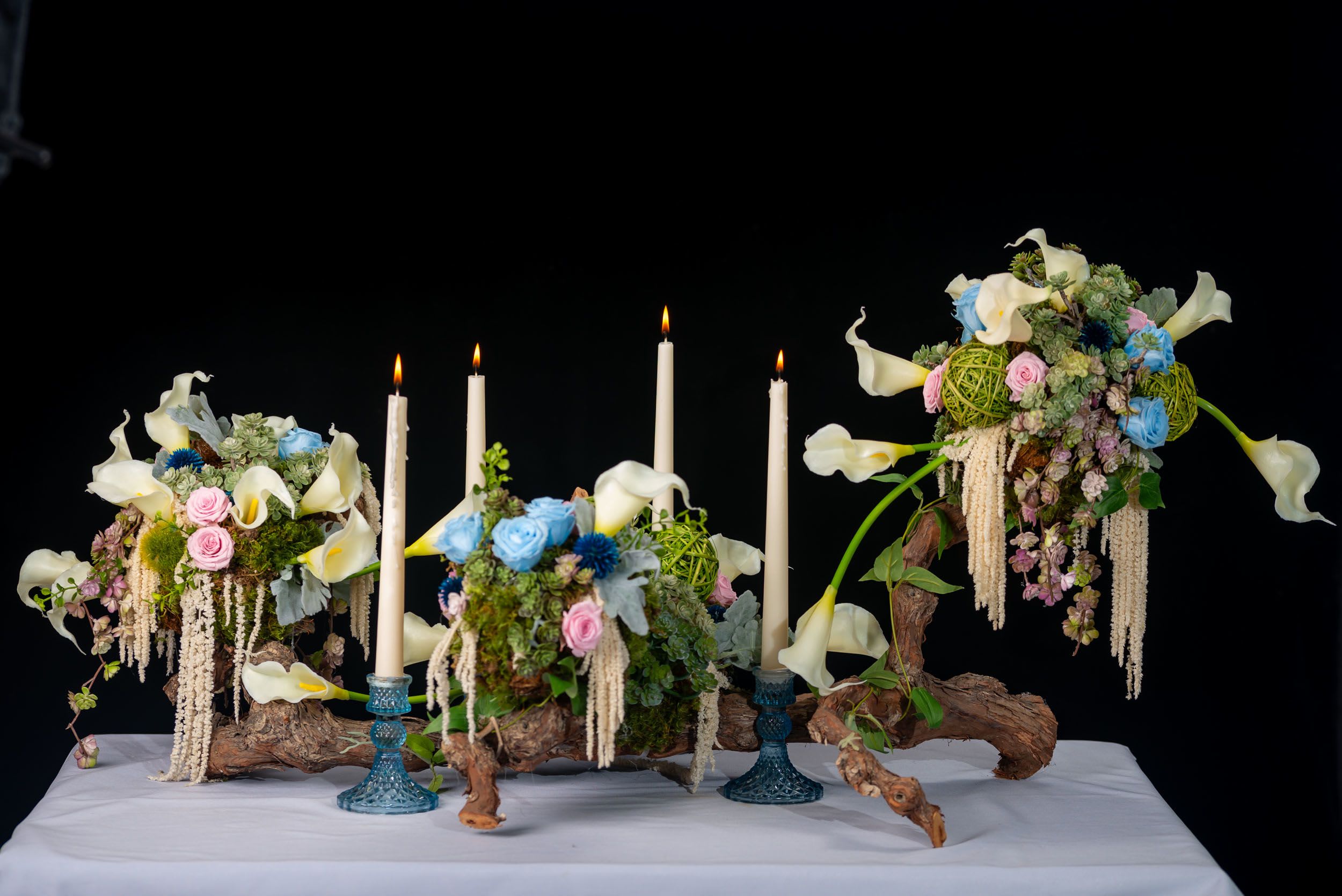 Three floral arrangements with white calla lilies and candles on driftwood bases