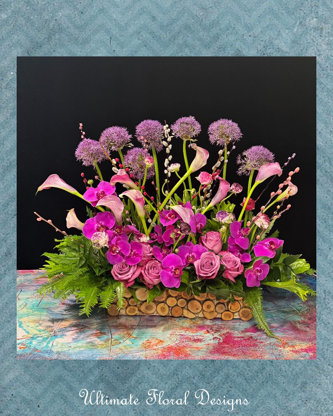 Pink and purple floral arrangement with calla lilies, orchids, and roses in a wooden container