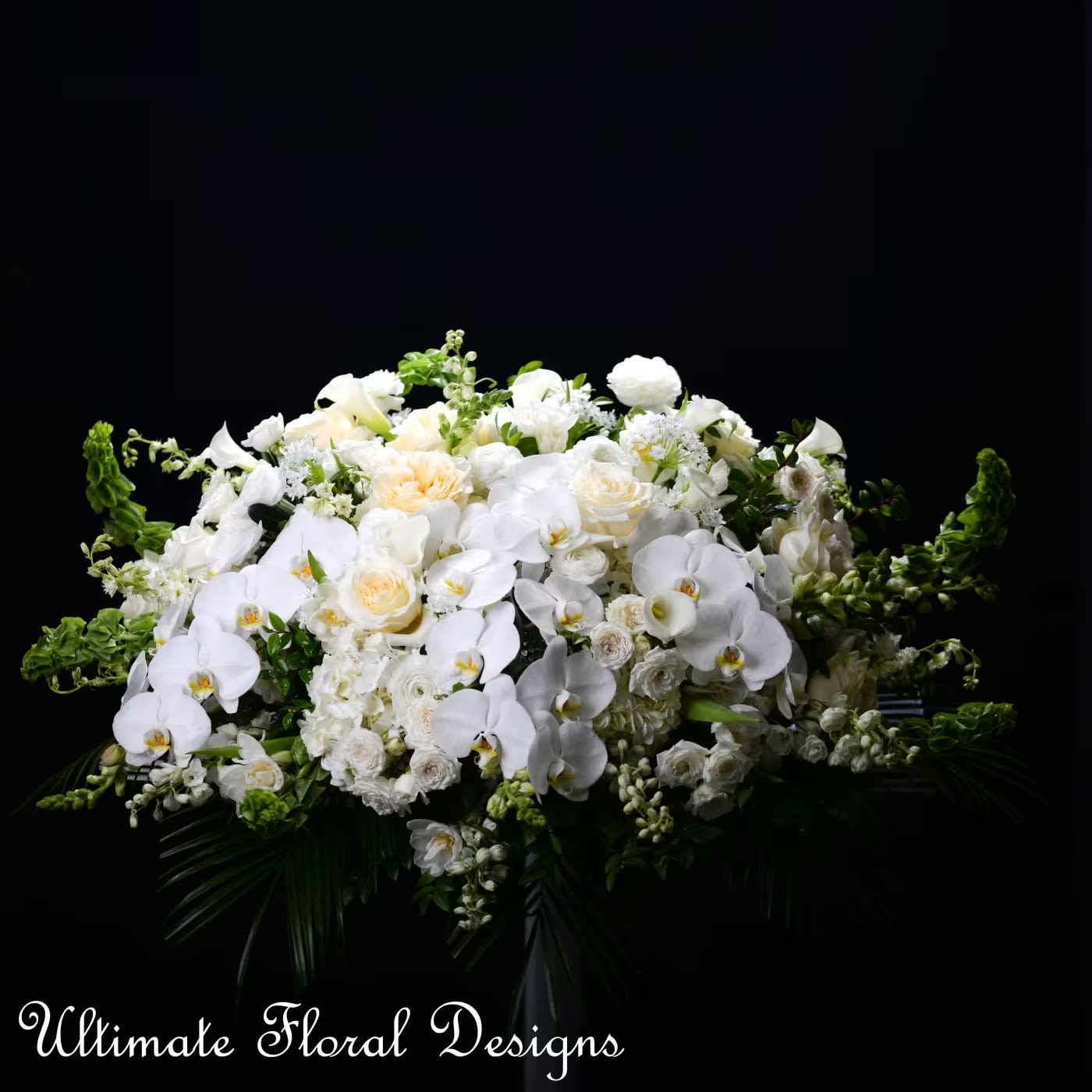 Eternal Peace -  "Eternal Peace" is a casket spray arrangement, beautifully crafted with white garden roses, orchids, and ranunculus,delphenium, accented with bells and green foliage. This all-white floral tribute symbolizes purity and serenity, making it a fitting homage for funerals and memorial services.