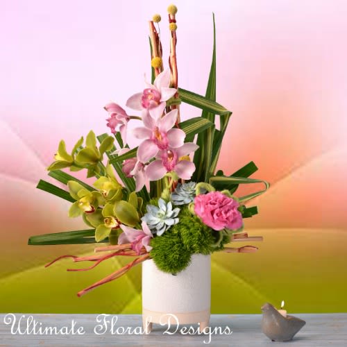 Pink and green orchid arrangement in a white vase with a small candle nearby