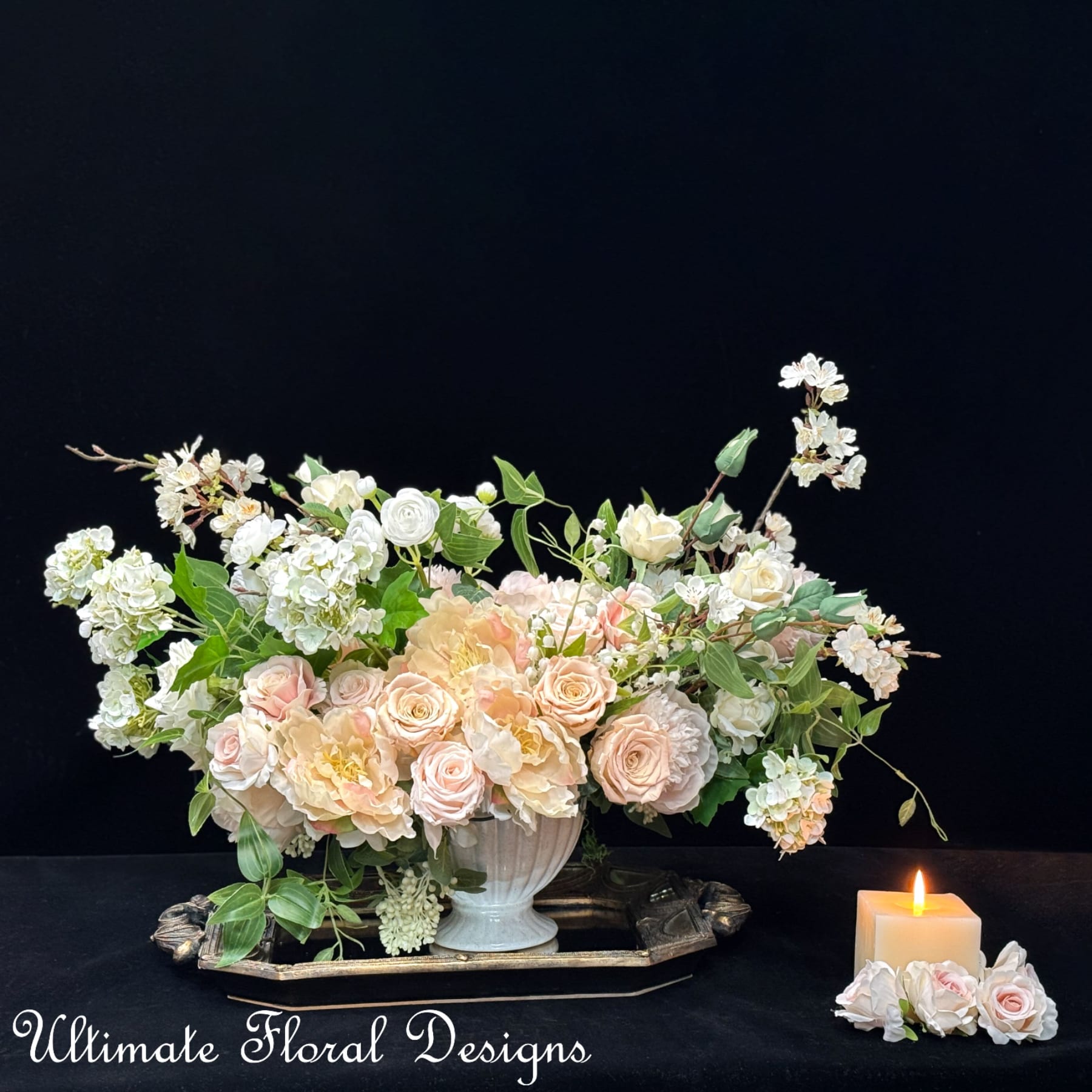 Pastel floral arrangement in a white vase with a lit candle beside it
