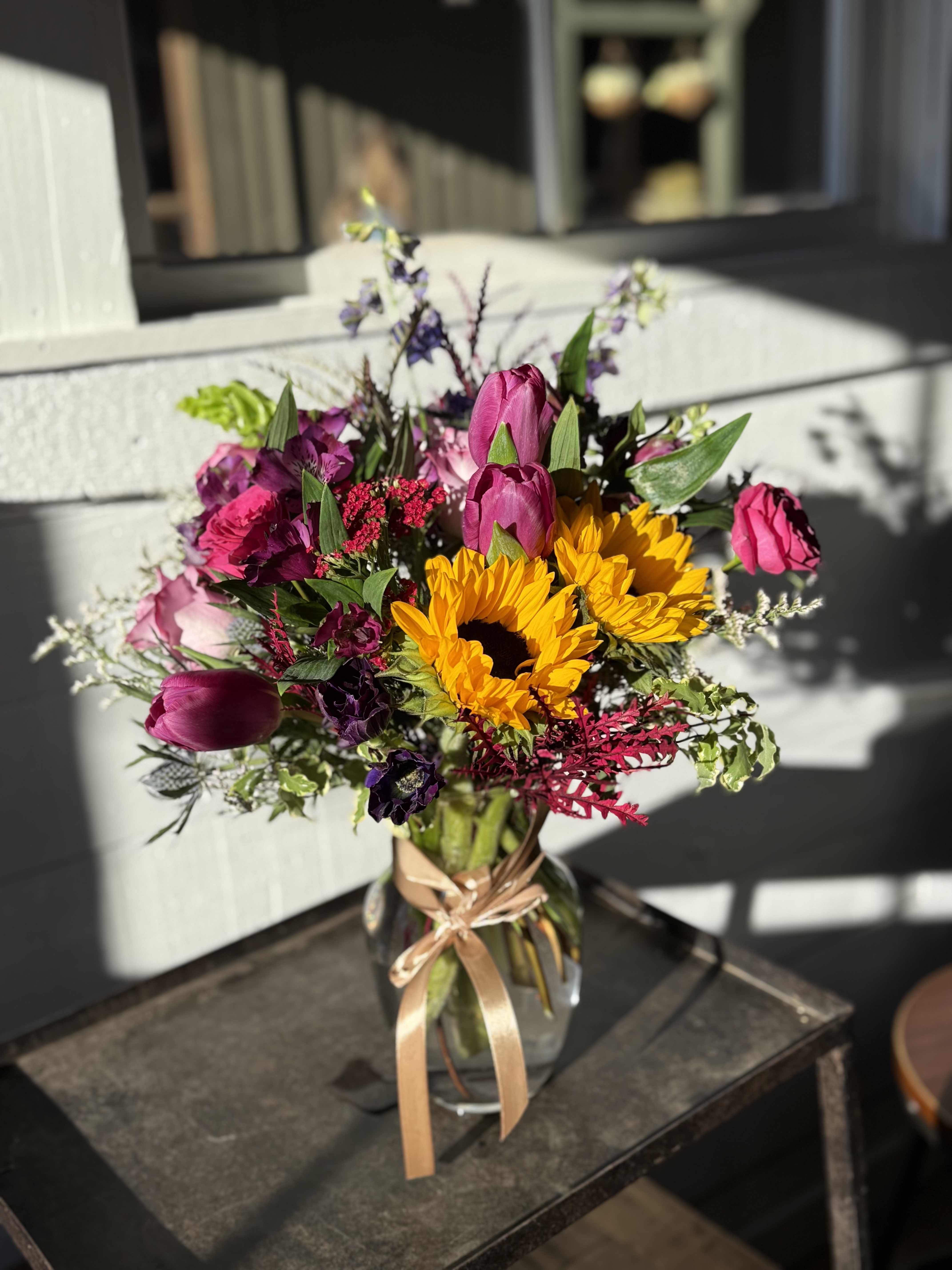 DESIGNER'S CHOICE - WILDFLOWER  - Mixed (SEASONAL) - This country wildflower–inspired arrangement brings the charm of open fields and simple country living into bloom.   A relaxed mix of meadow-style flowers, soft textures, and fresh greenery is loosely arranged for a natural, gathered-from-the-garden feel.   Warm, cheerful, and unpretentious, this design feels right at home in any space—perfect for sending comfort, sharing a smile, or adding a touch of rustic beauty to the day.  *SEASONAL - FLOWERS MAY VARY DUE TO AVAILABILITY. 