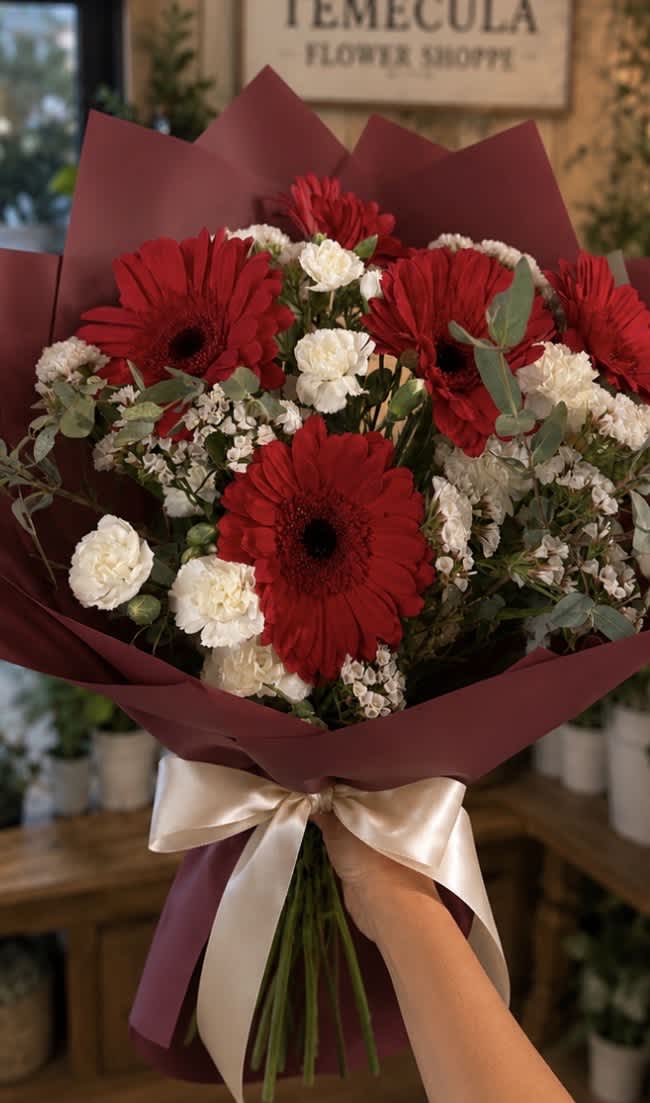 Bouquet of red gerbera daisies and white carnations wrapped in burgundy paper