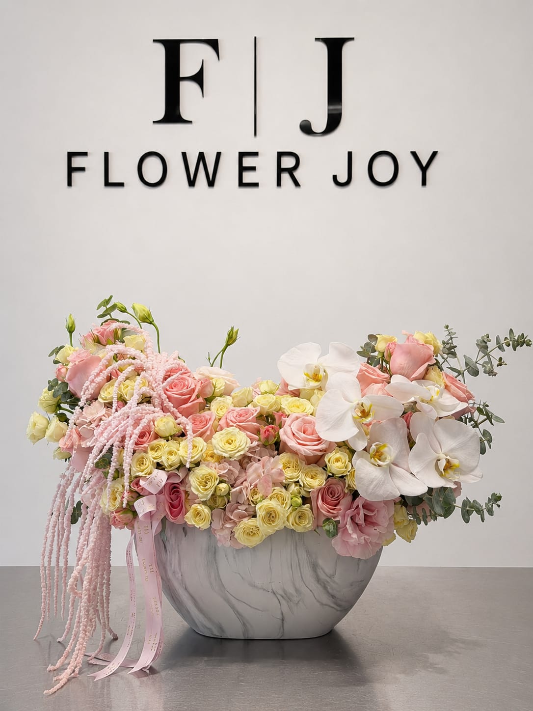 Blush Orchid Cascade - A luxurious arrangement of blush roses, soft yellow spray roses, white orchids, hydrangeas, and cascading pink accents, beautifully displayed in a modern marble-style vase. Elegant, romantic, and artistic, perfect for anniversaries, birthdays, engagements, or unforgettable celebrations.
