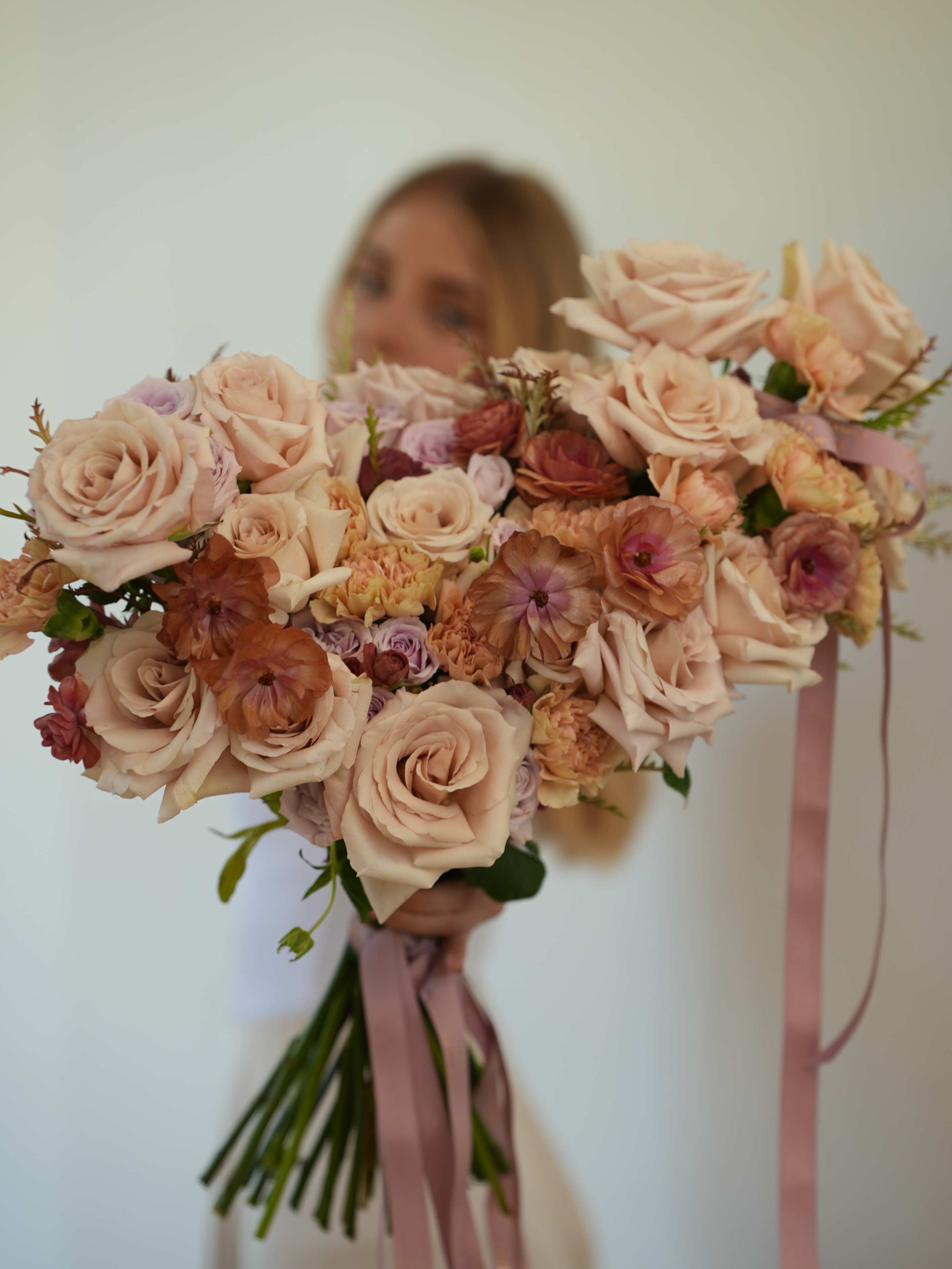 Large bouquet of blush roses and peach flowers tied with pink ribbon