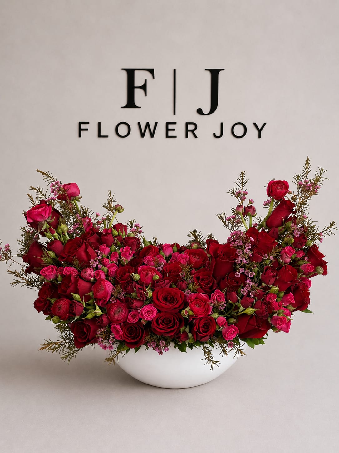 Crimson Romance Garden - A dramatic arrangement of deep red roses, vibrant pink spray roses, ranunculus, delicate wax flowers, and textured greenery, beautifully displayed in a modern white vase. Bold, romantic, and unforgettable, perfect for anniversaries, proposals, Valentine’s Day, or grand celebrations.