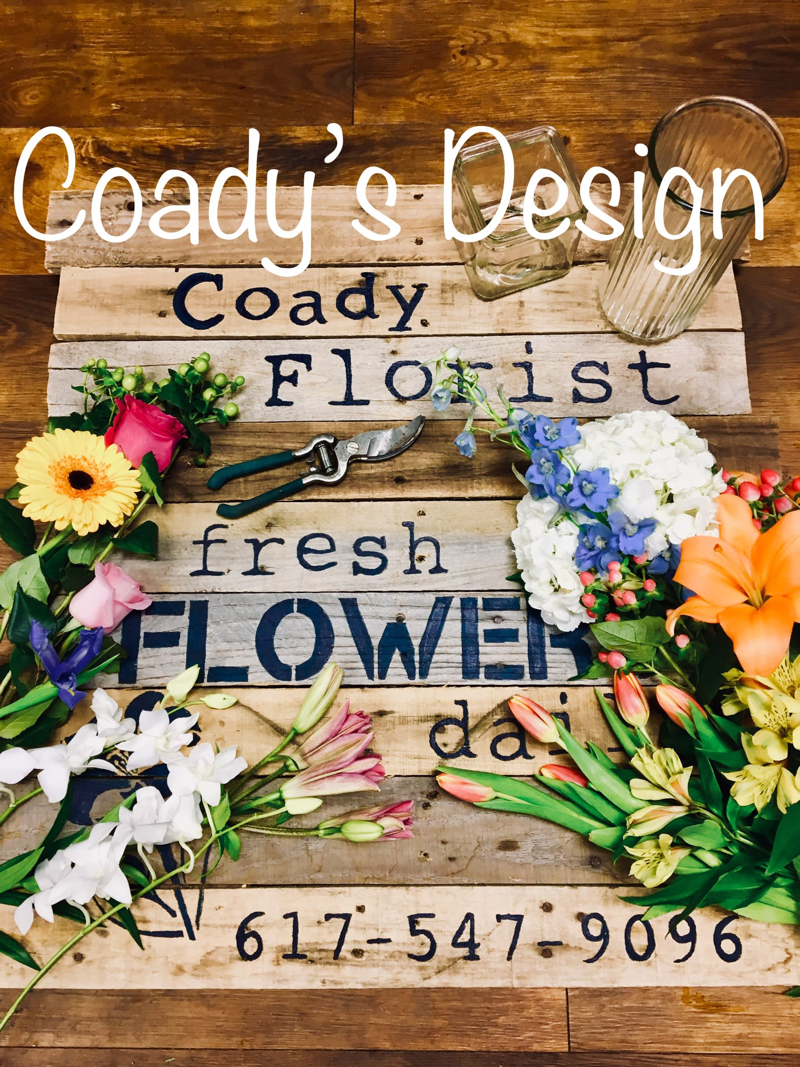 Assorted flowers arranged around a wooden sign with glass vases