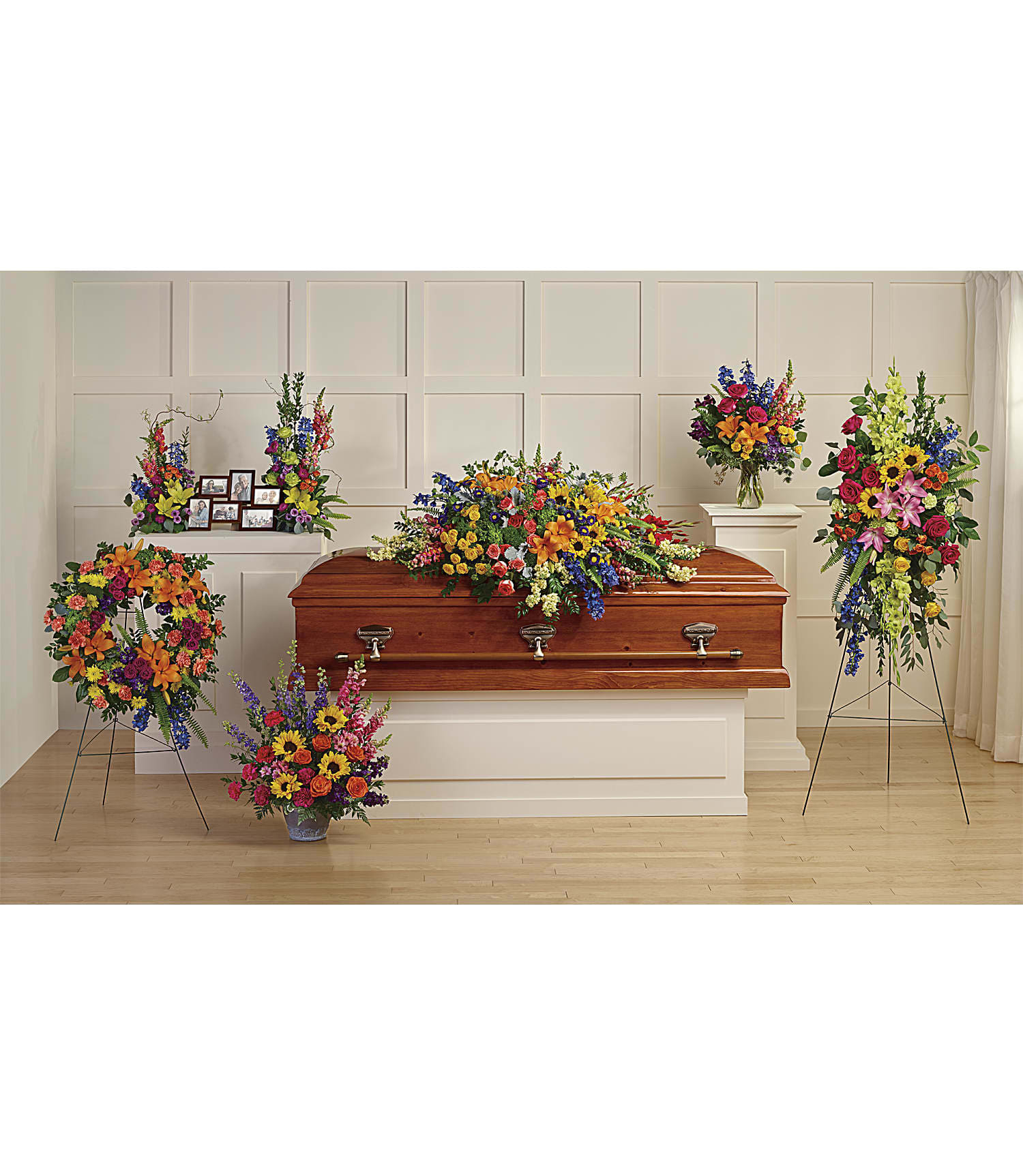 Colorful funeral casket spray with standing floral tributes around a wooden casket