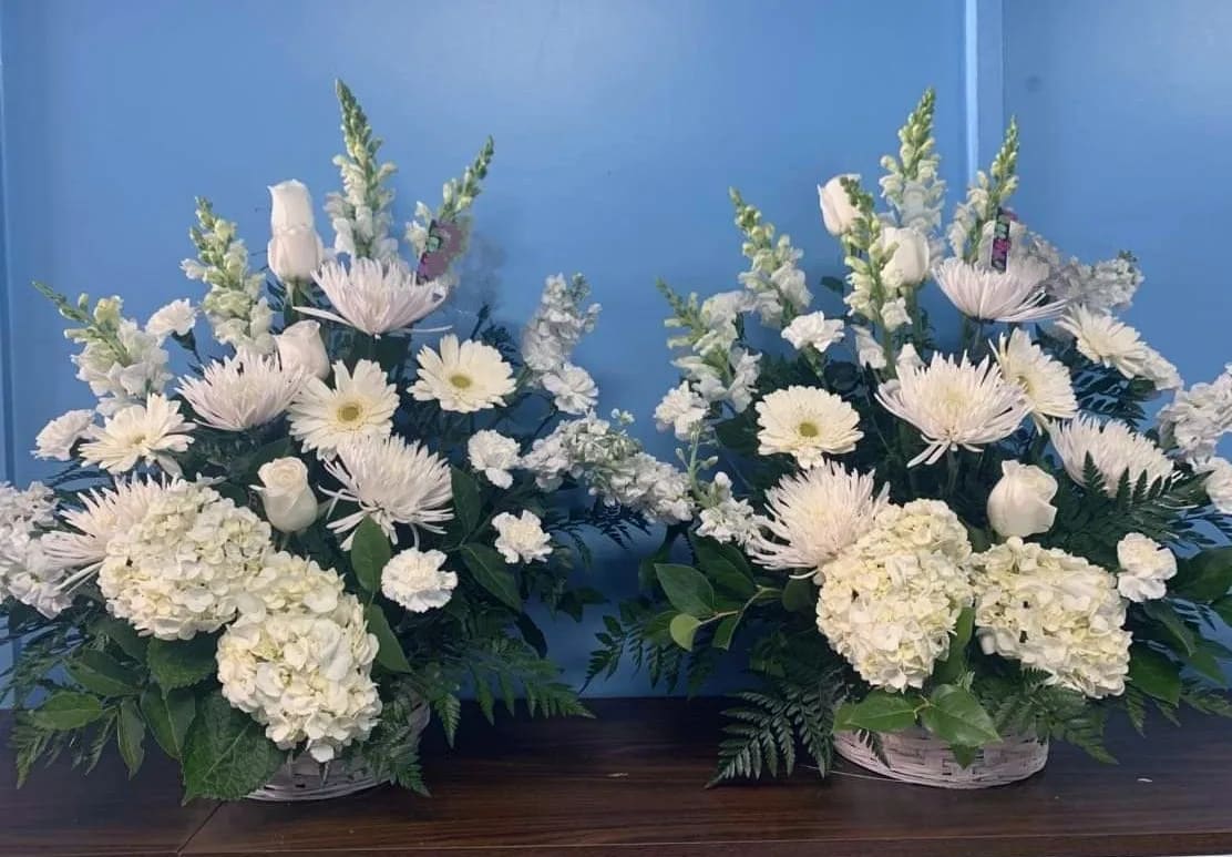 Two white floral arrangements in baskets with daisies and hydrangeas
