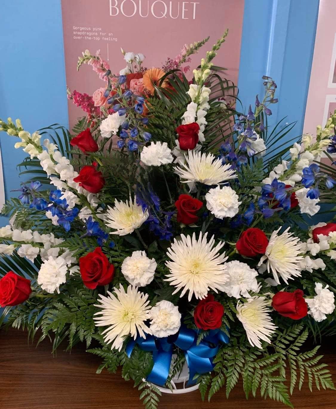 Large red, white, and blue floral arrangement in a basket with a blue ribbon