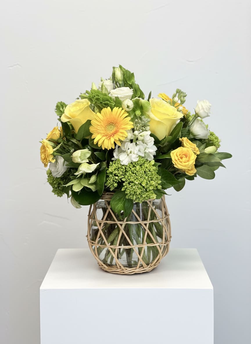 Yellow and white flower arrangement in a glass vase with wicker wrap