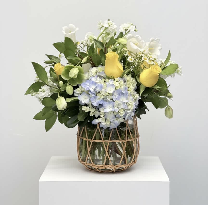 Yellow roses and blue hydrangeas in a glass vase with woven wrap
