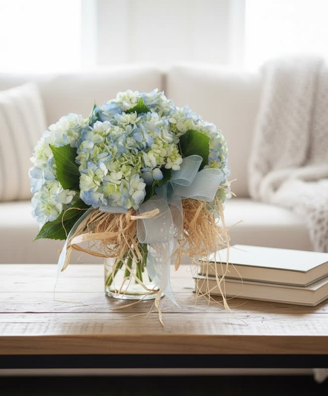 Carnton Hydrangea Cluster in blue - Inspired by the hydrangeas that line the fences near the gardens of Carnton Plantation in Franklin, Tennessee... this design features pale blue hydrangeas, hand gathered and clustered together and place in a simple vase on a bed of riverstones.. accented with a simple ribbon and raffia.