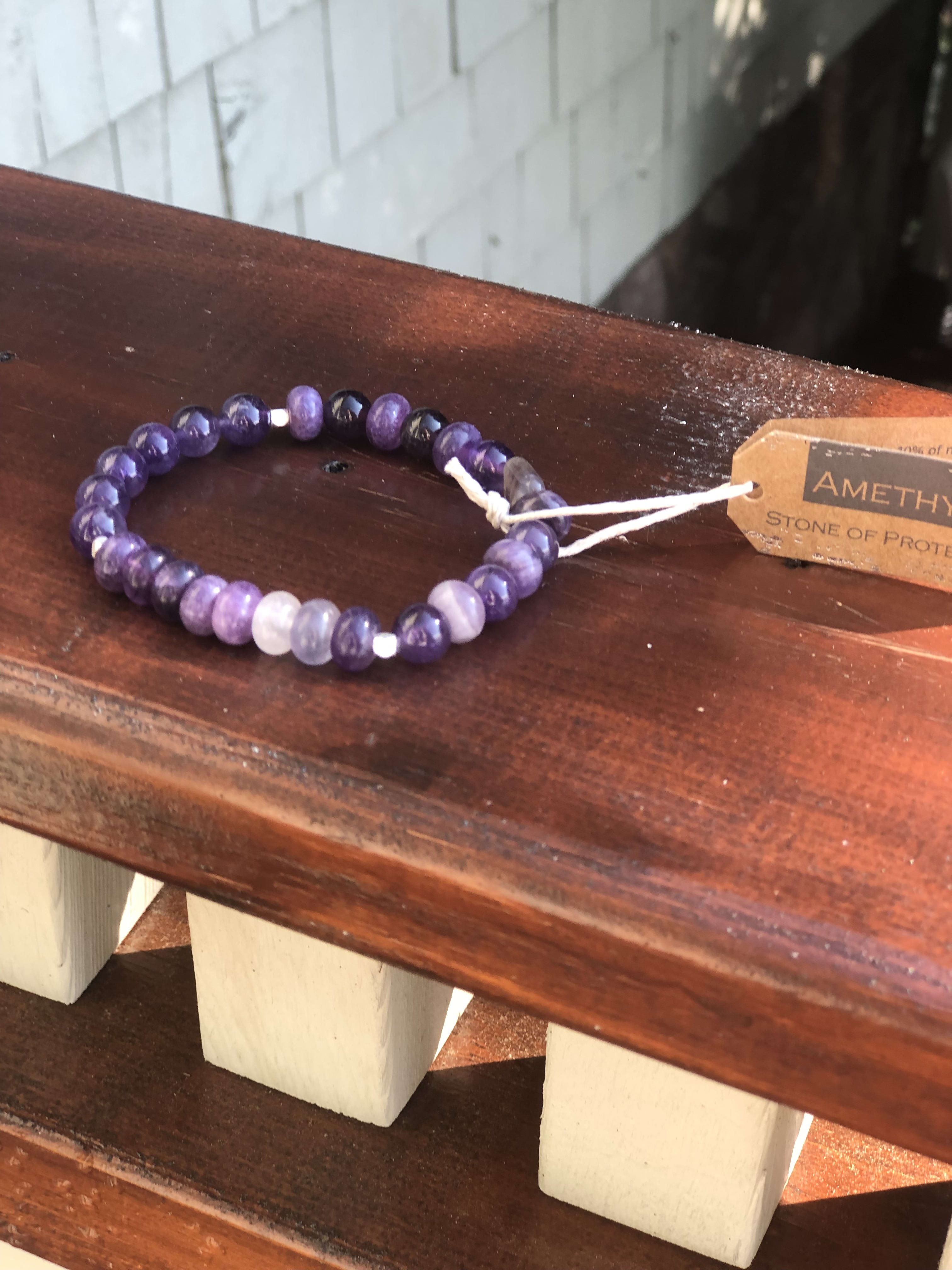 Purple beaded bracelet on a wooden shelf with a paper tag